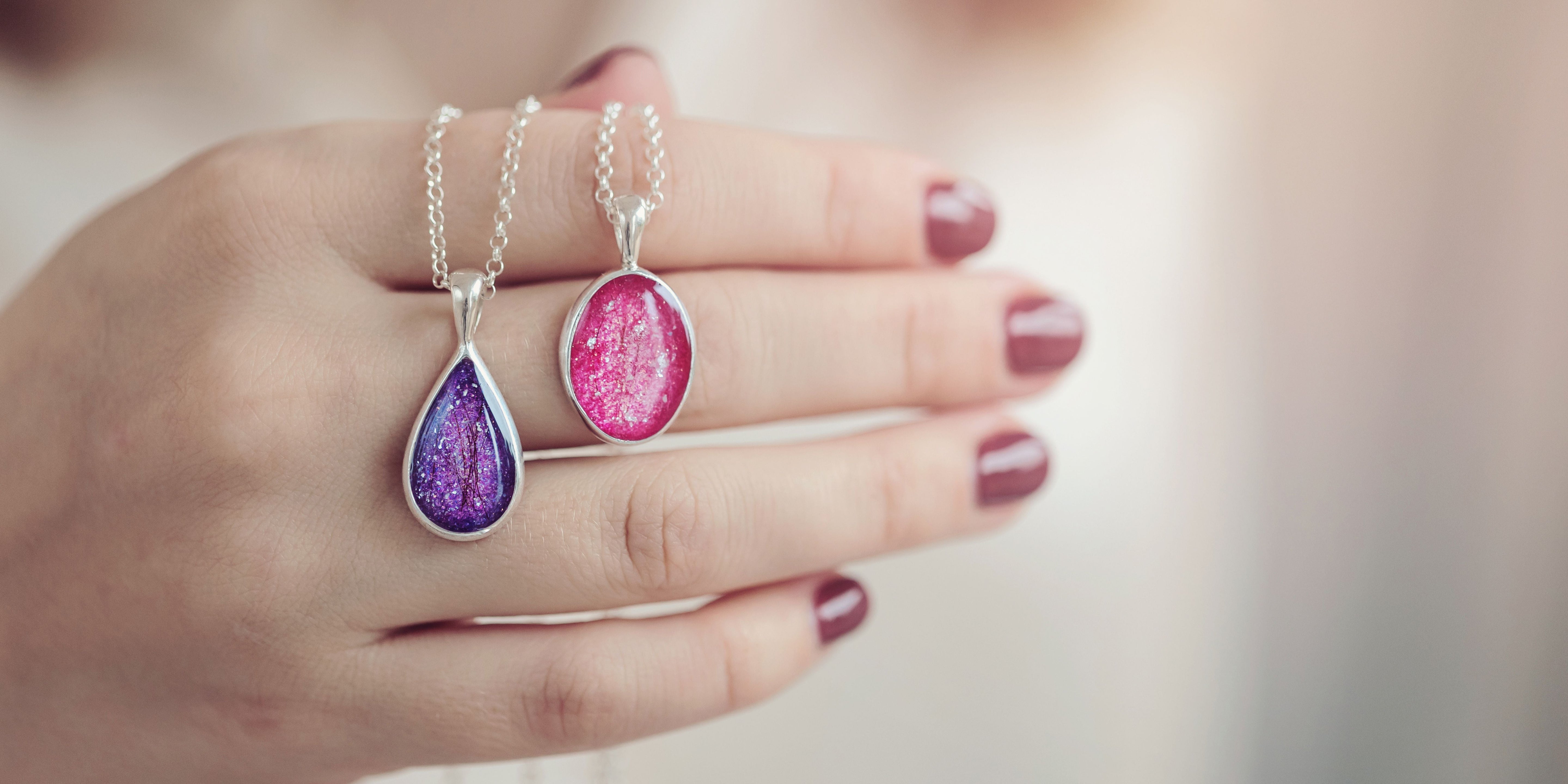 A woman holding two memorial pet hair necklaces in purple and pink.