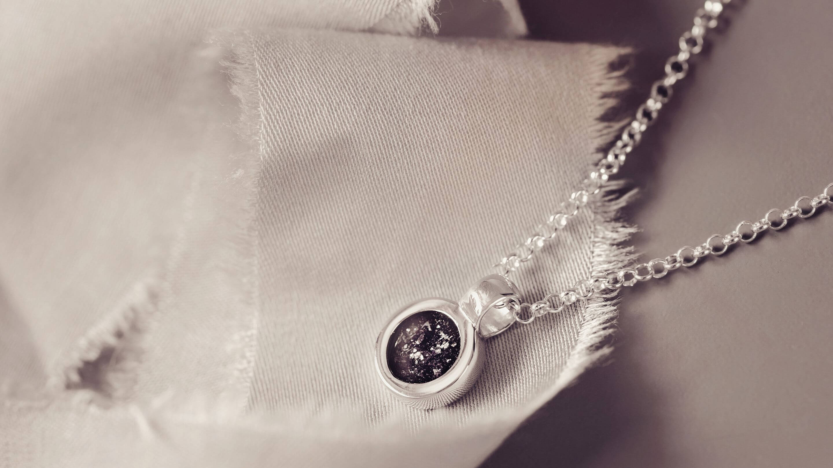 A silver necklace with a round charm, created using cremation ashes