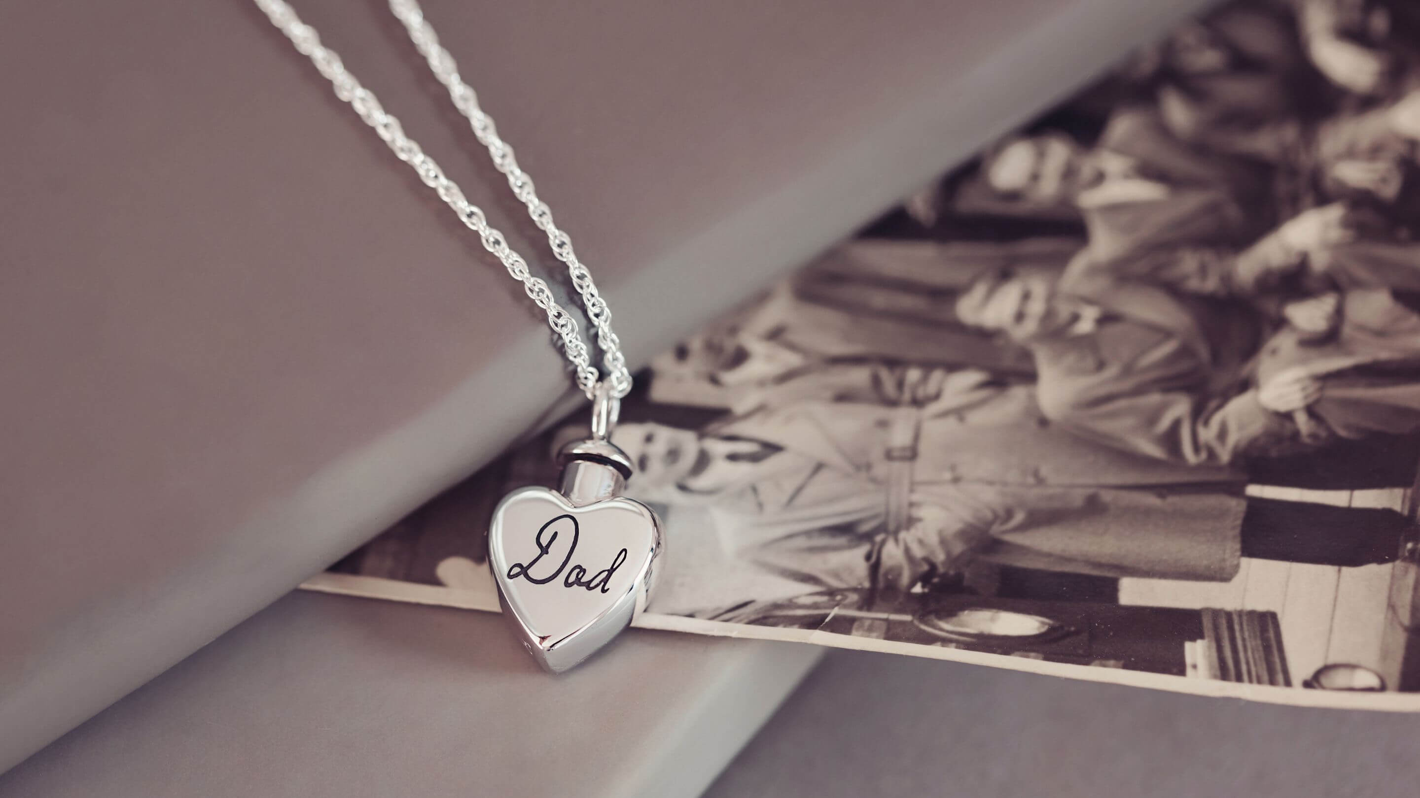 a silver Cremation Ashes Self-Fill Heart Urn Necklace with 'Dad' engraved on the front.