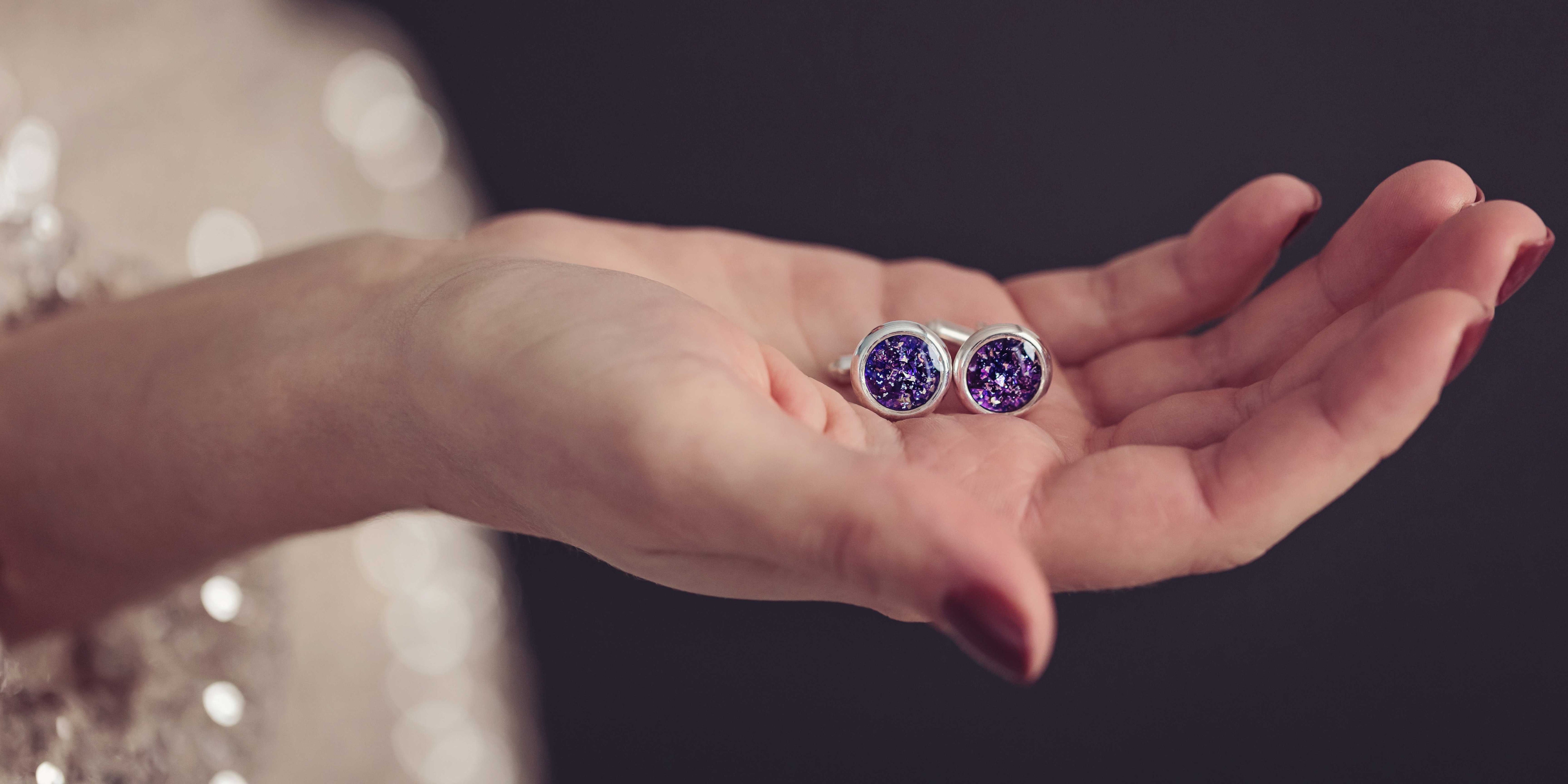 A lady holding a set of Pet Ashes Cufflinks in purple