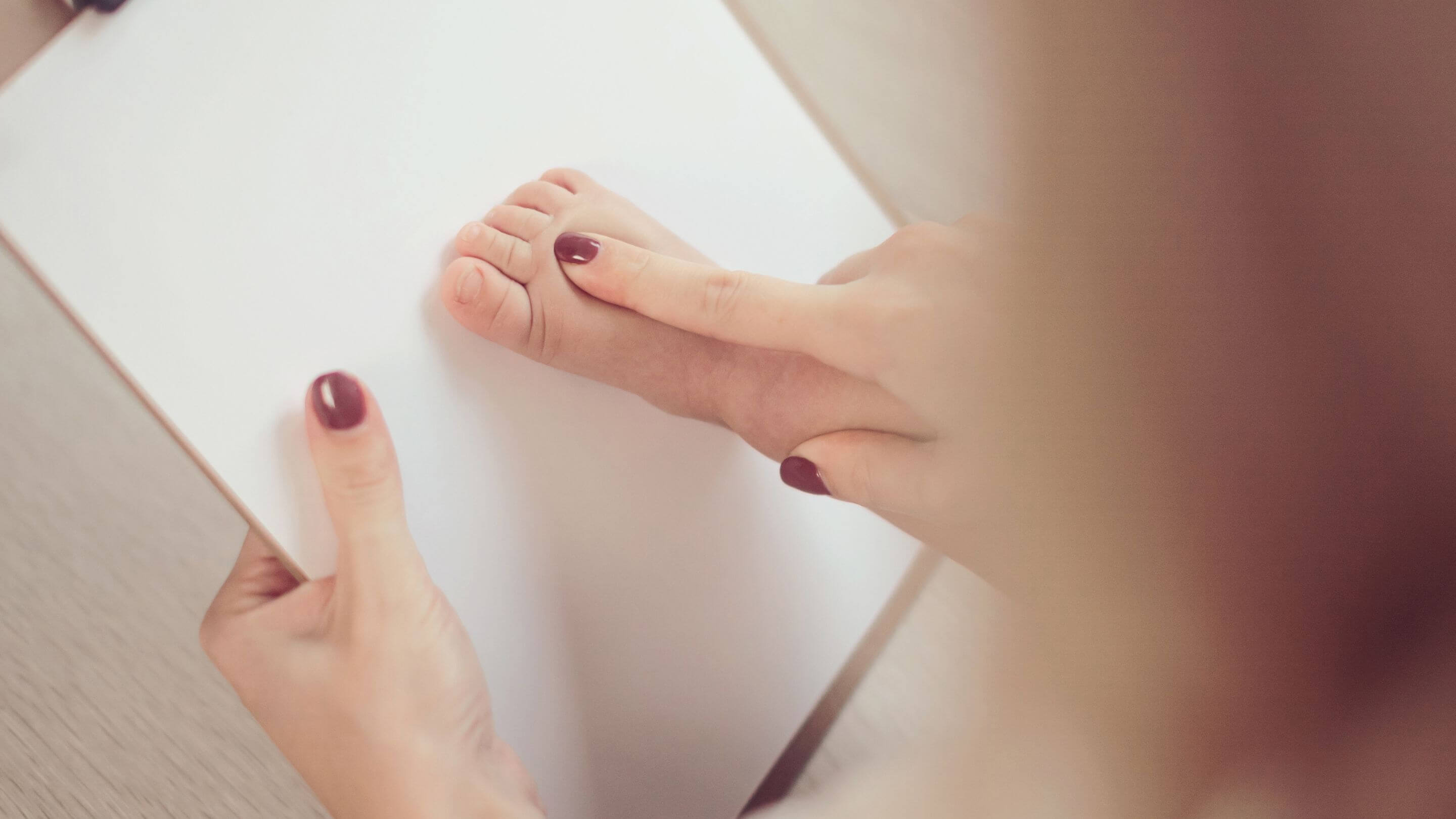 A women with painted nails using an inkless print kit to take a toddlers footprint