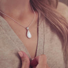 Lady modelling a teardrop shaped necklace in a clear colour filled with Cremation Ashes 