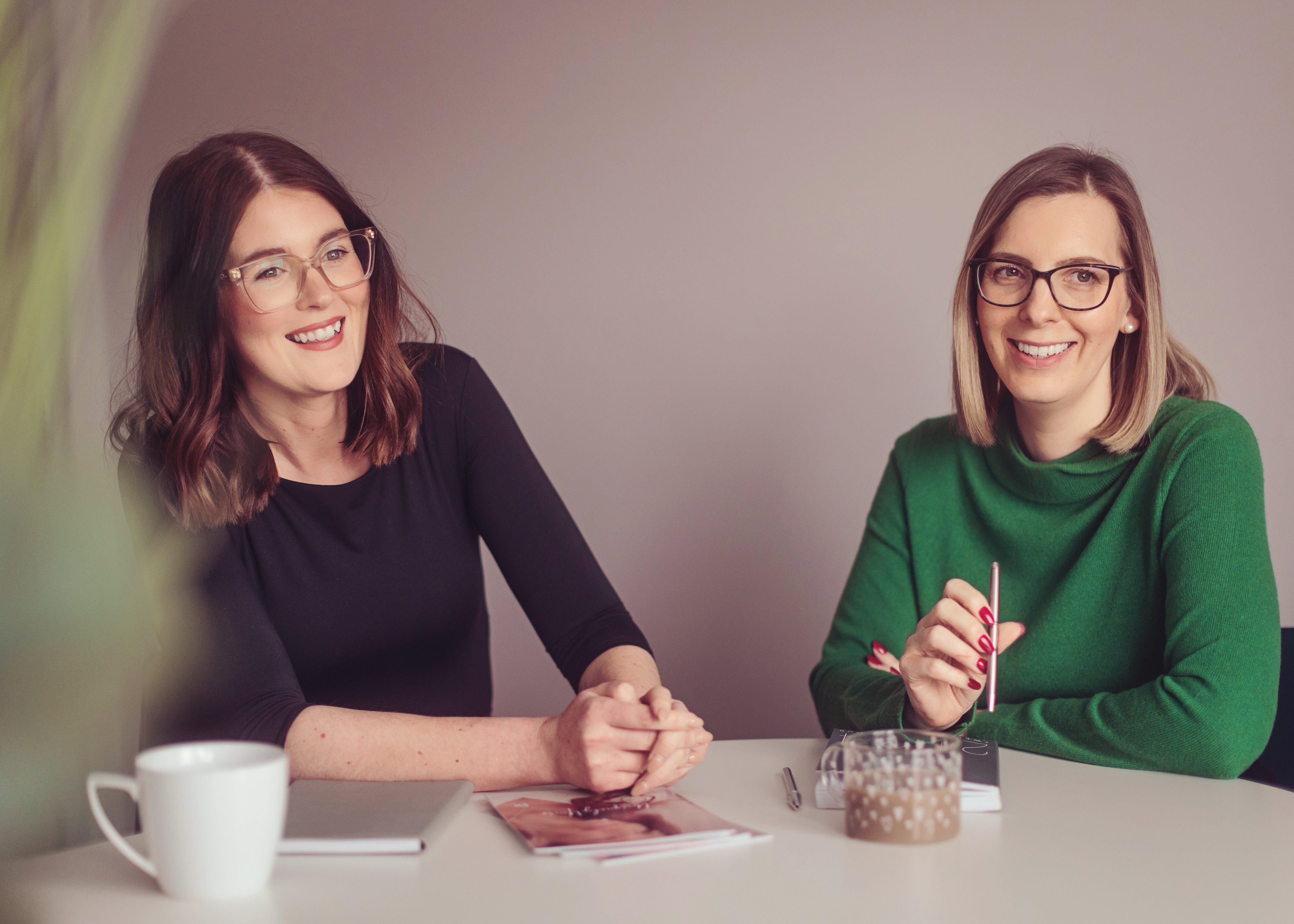 Two team members engaged in conversation at a table, each with a cup of coffee