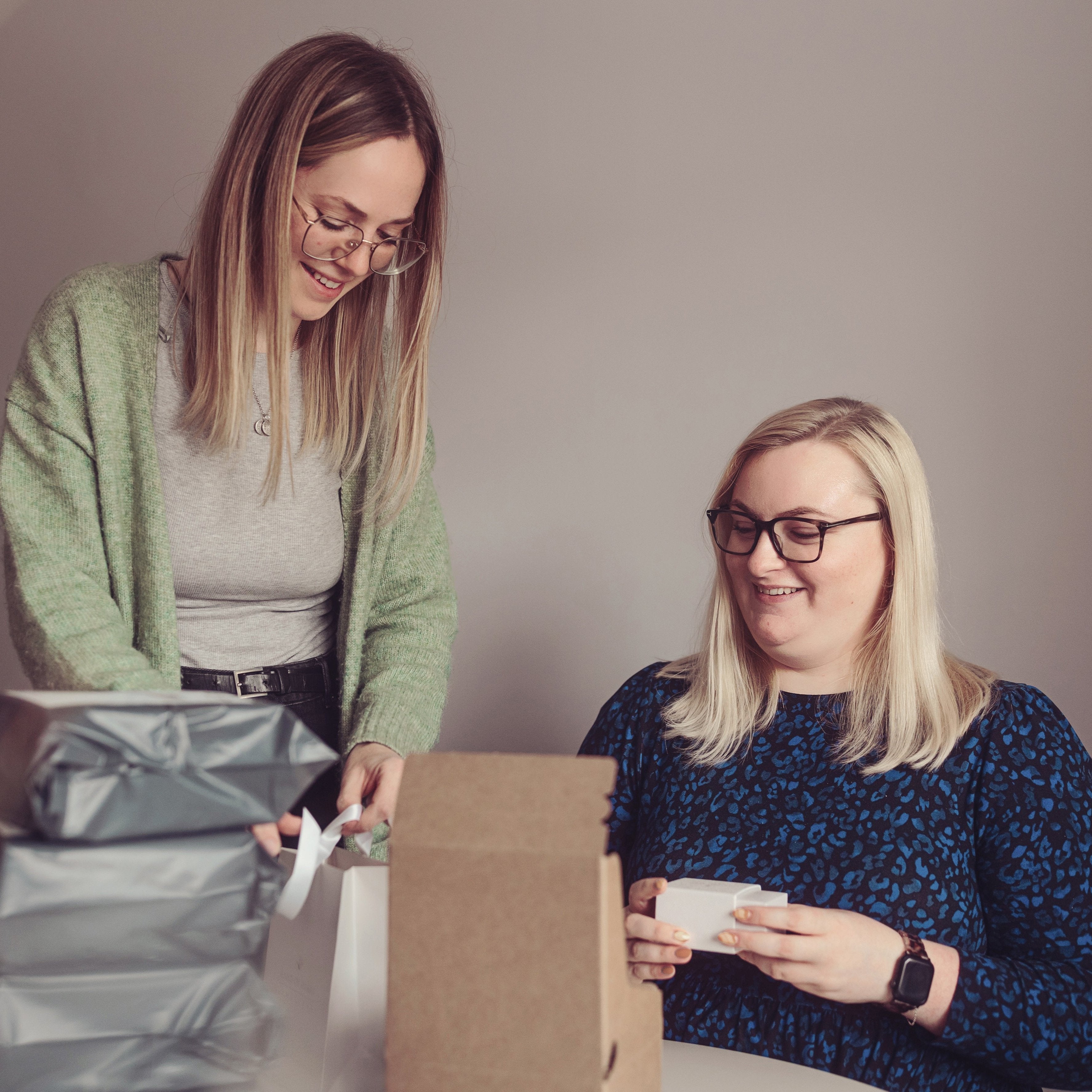 Two team members working together on packaging. One is standing and organising, while the other is seated holding a white jewellery box