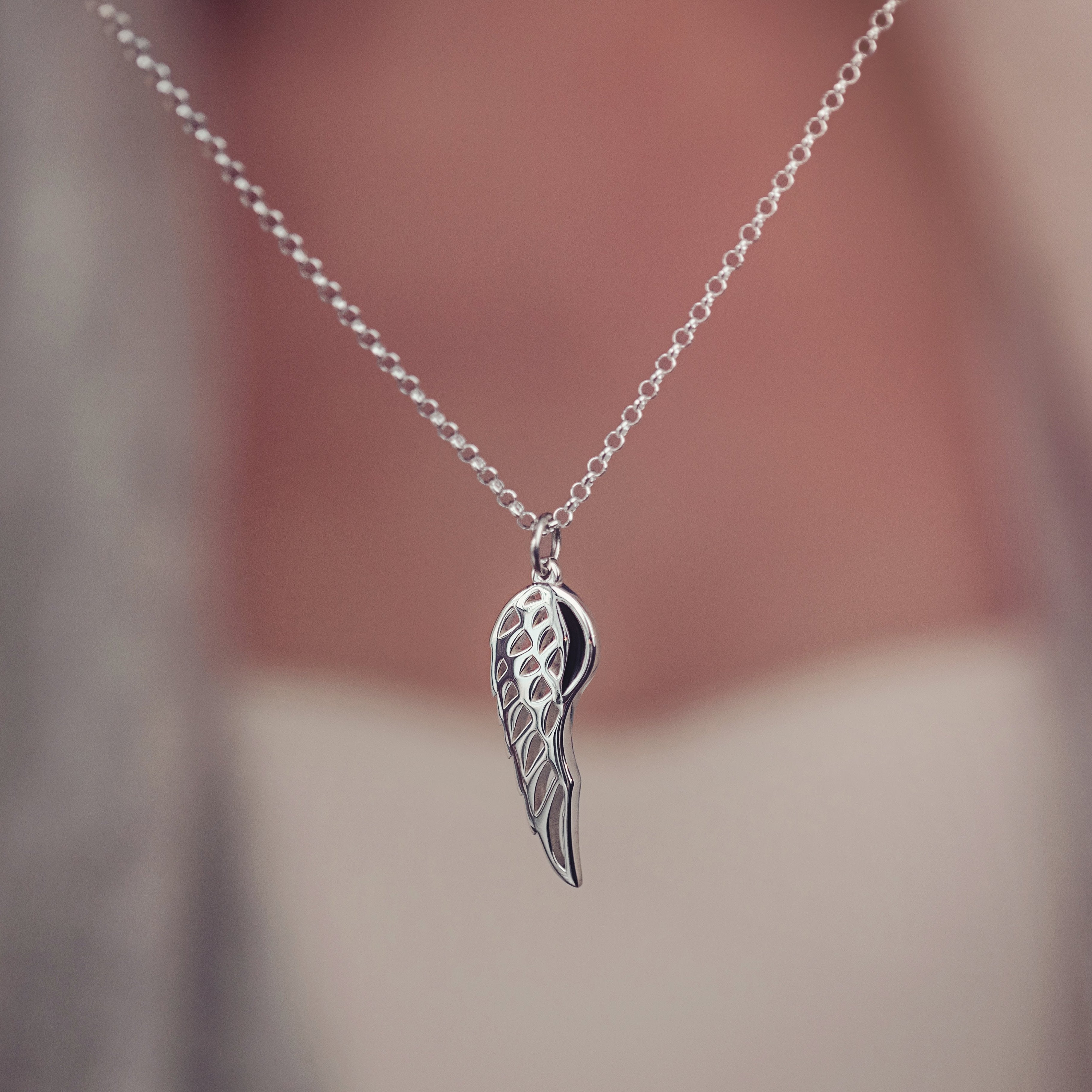 A silver angel wing necklace hanging, holding cremation ashes 