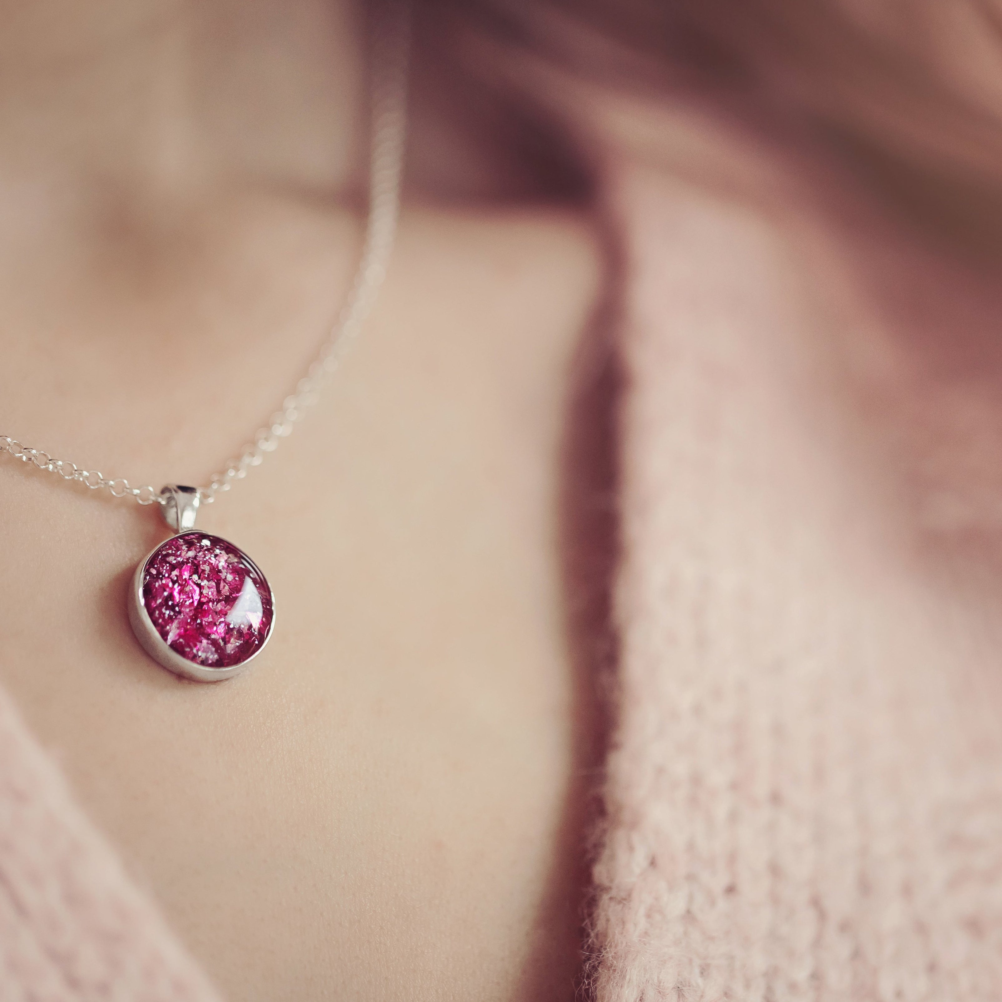 A close up of a woman in a pink jumper wearing a pink cremation ashes round necklace 