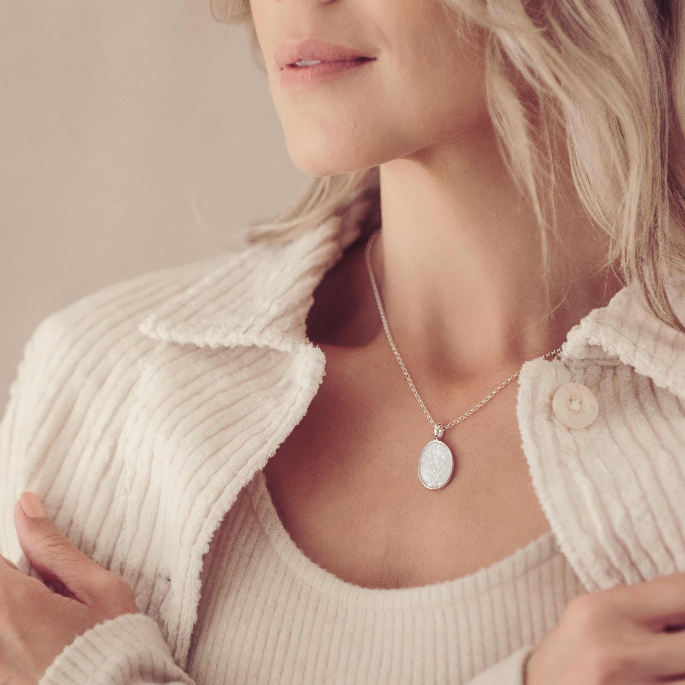 an image focussed on a blonde lady's neckline as she wears a silver oval necklace filled with cremation ashes