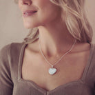 A lady's neckline wearing a large silver necklace containing cremation ashes, the lady is wearing a brown top and has blonde hair