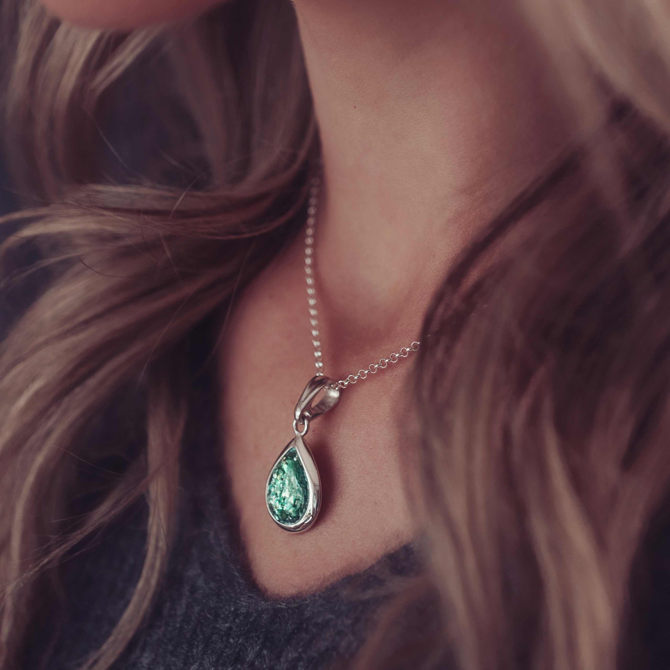 A green ashes necklace being worn on a lady with long brown hair