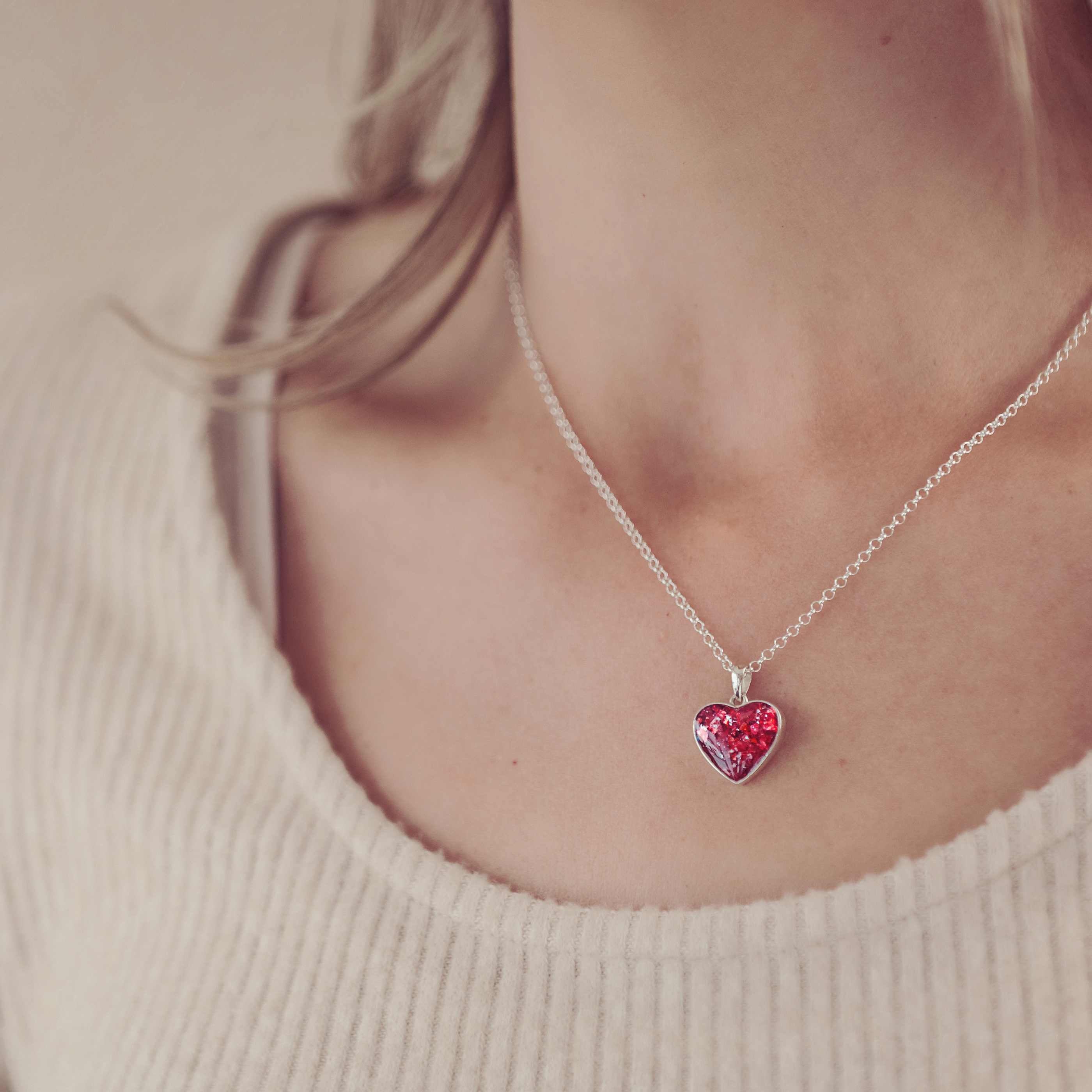 image of a lady's neckline while she's wearing a silver cremation ashes necklace in a red colour. 