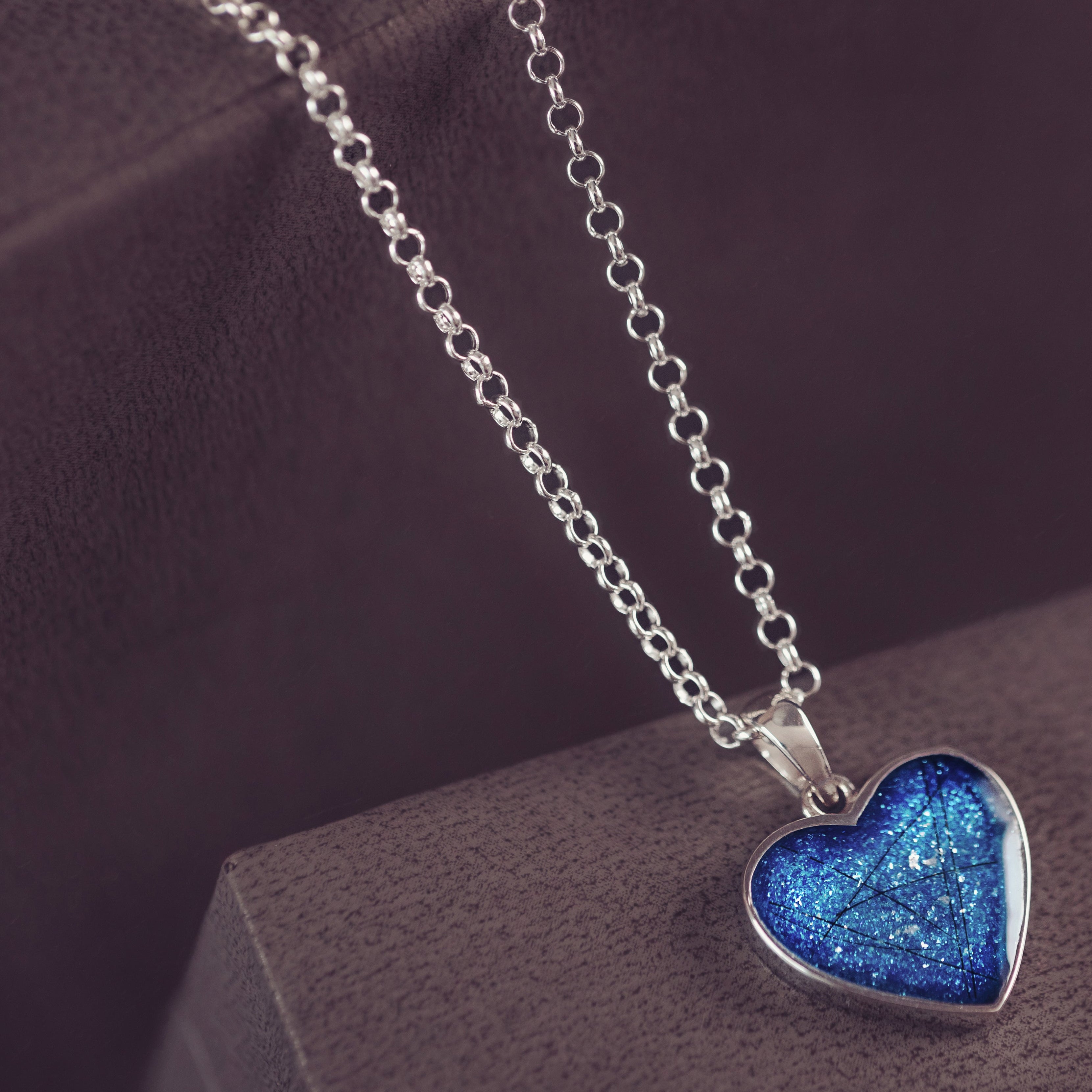 A blue small heart necklace containing hair on a silver chain