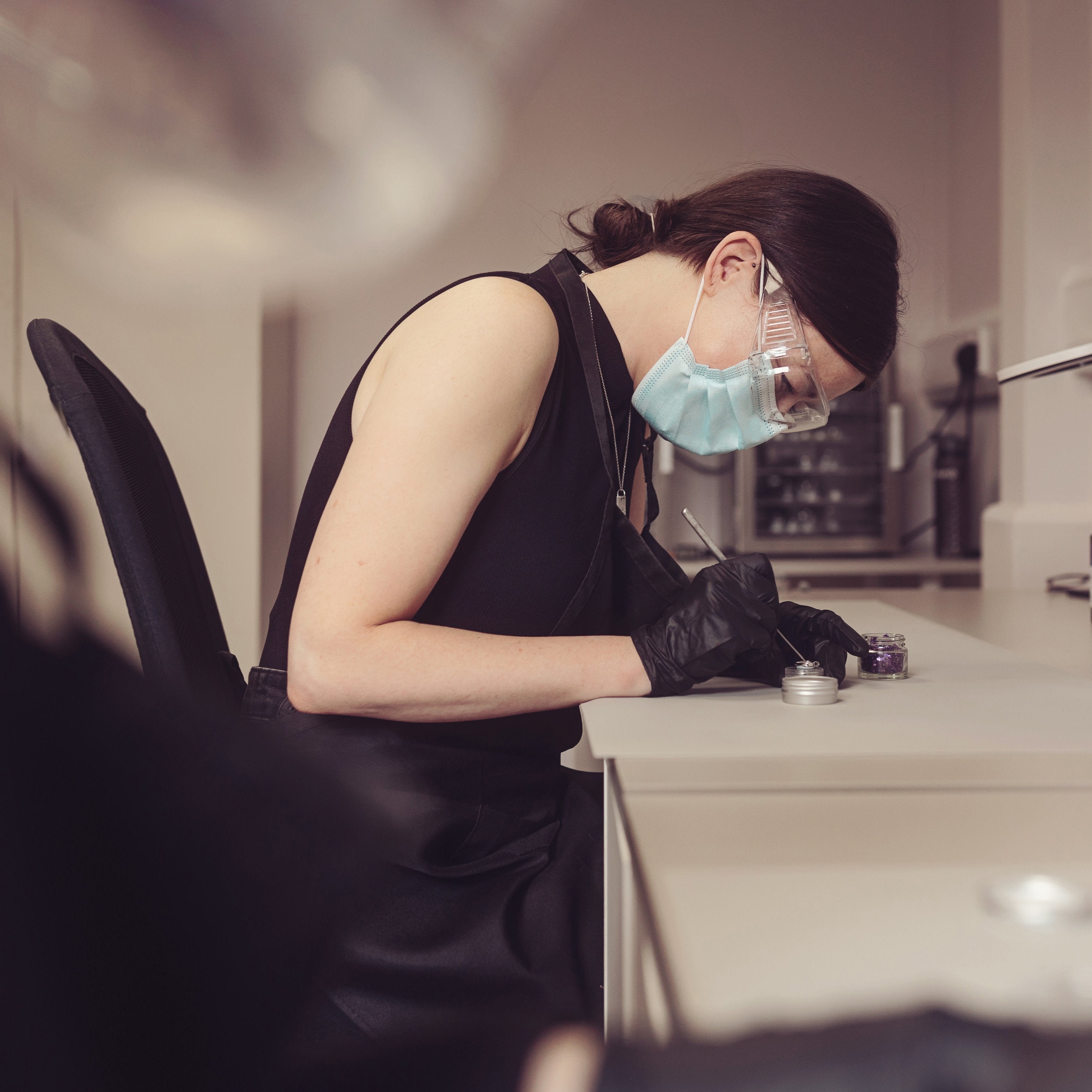 Jewellery designer wearing protective gloves, glasses, and a mask while carefully crafting a memorial piece with ashes