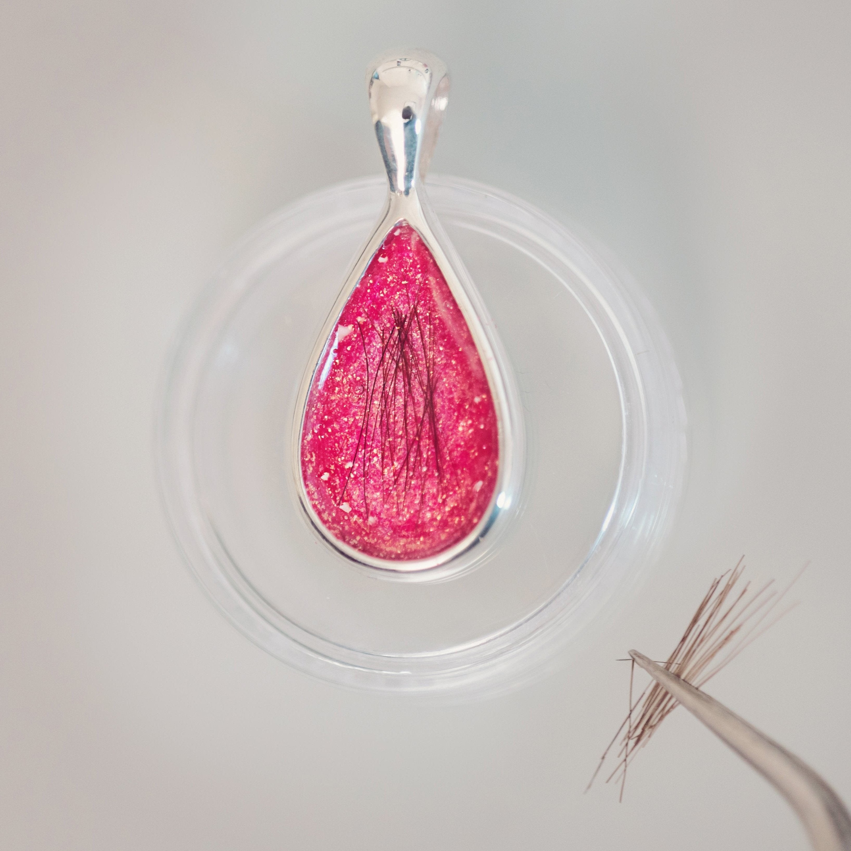 Close up of the memorial teardrop necklace in coral, showing a loved one's hair being intricately placed into the pendant using tweezers