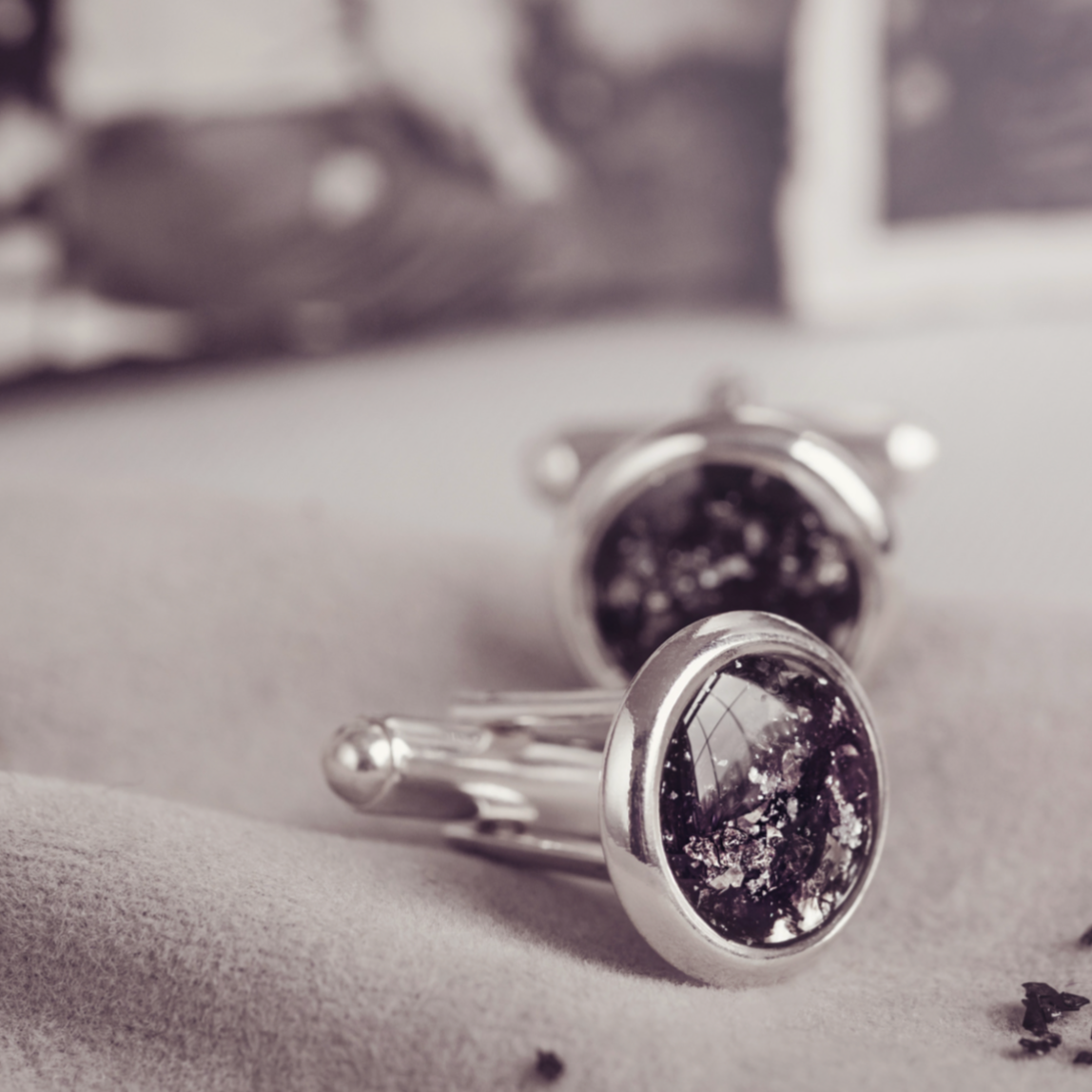 A close up of a pair of black cufflinks containing cremation ashes, featuring a black and white photo blurred in the background