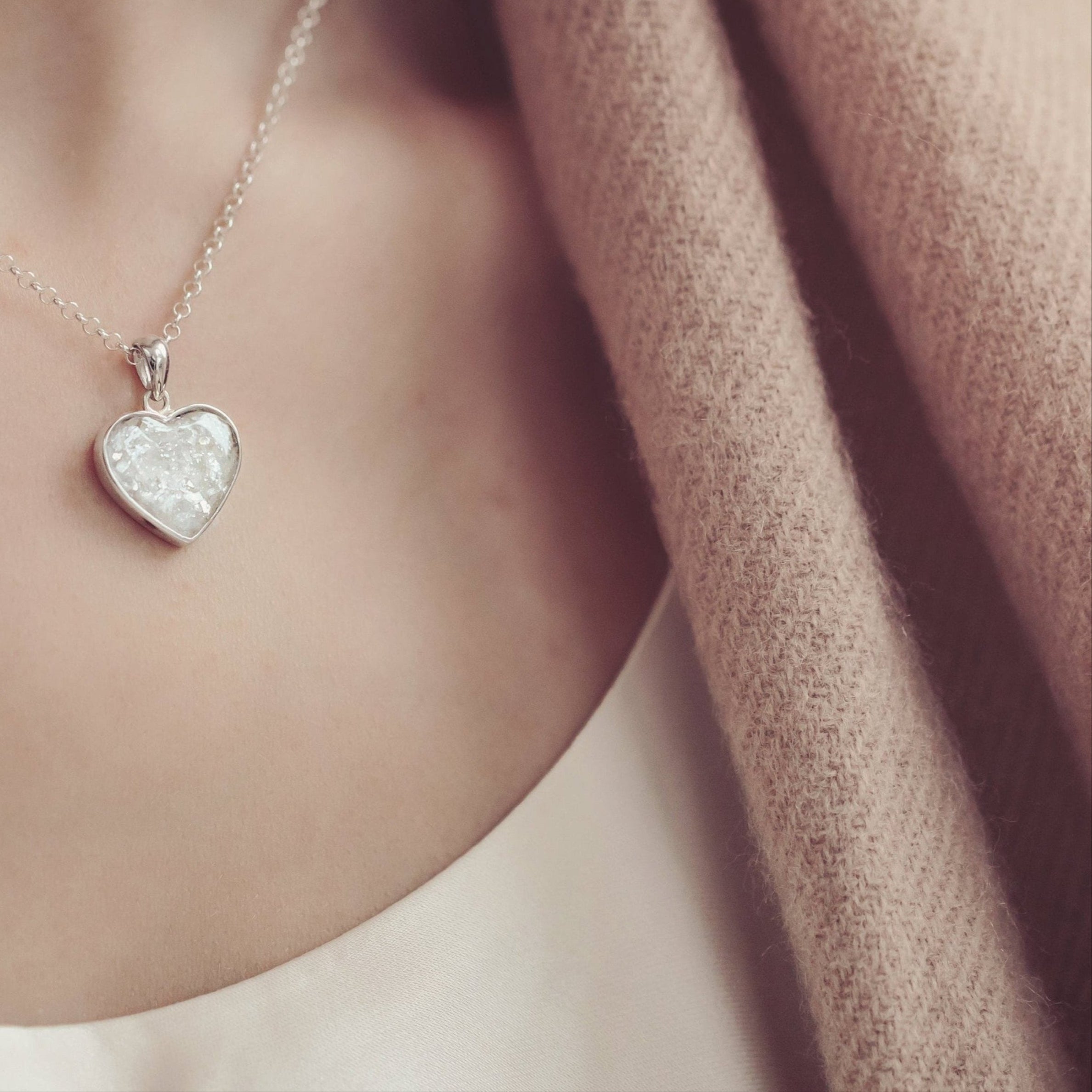 Woman dressed in a white top and beige scarf, wearing a clear heart necklace containing cremation ashes