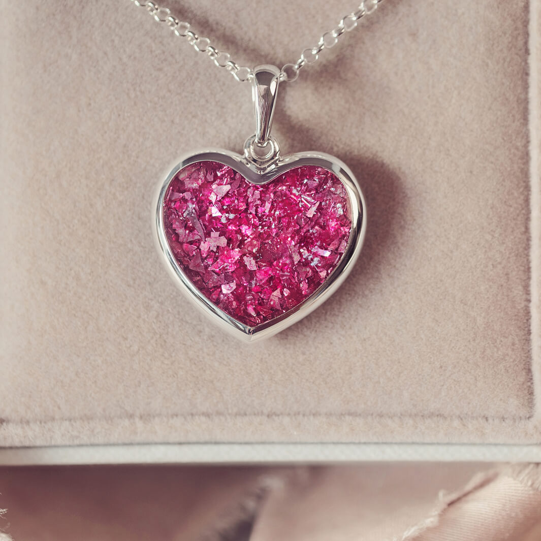 A sterling silver large heart pendant, hanging on a sterling silver belcher chain. The centre of the heart is filled with pink crystal and ashes.