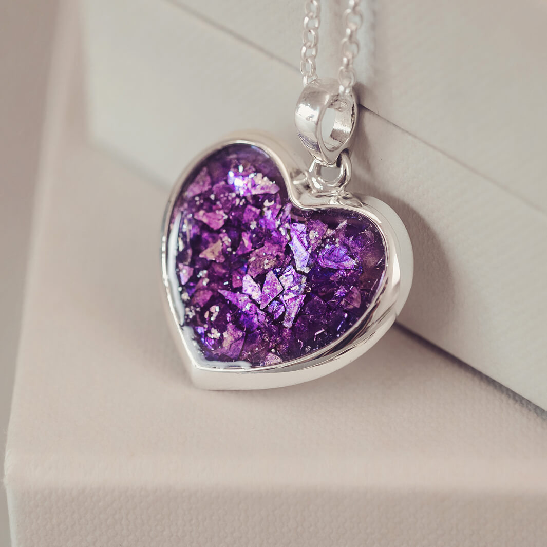 Sterling silver Large Heart necklace with a central section filled with memorial ashes and purple crushed crystals, displayed on a beige background.