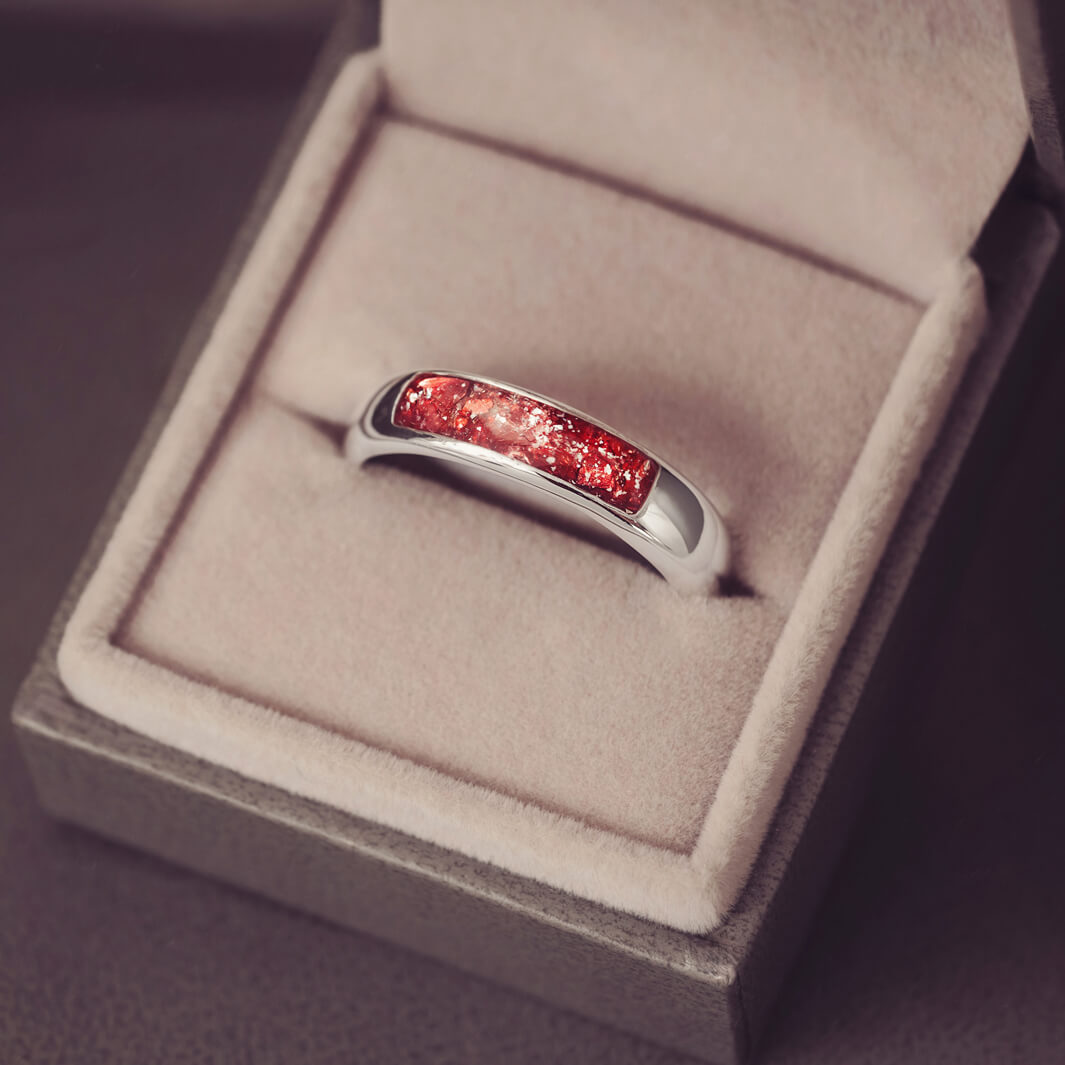 Sterling silver Mens Band Ring with a central section filled with memorial ashes and red crushed crystals, displayed in a grey jewellery box