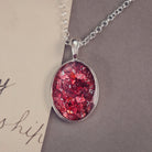 An oval shaped sterling silver pendant, on a silver belcher chain, filed with red crushed crystal and cremation ashes