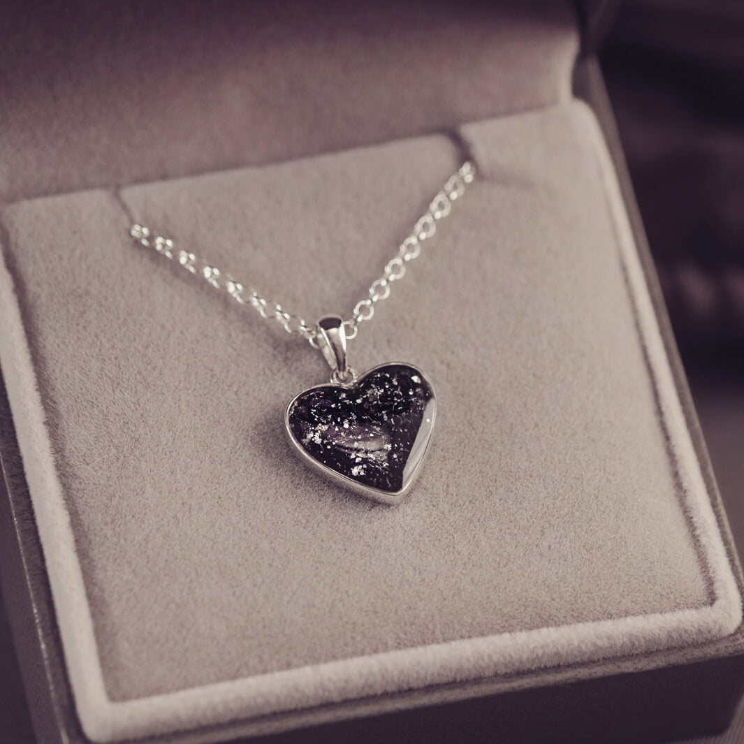 Sterling silver heart necklace with a central section filled with memorial ashes and black crushed crystals, displayed in a grey jewellery box