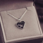 Sterling silver heart necklace with a central section filled with memorial ashes and black crushed crystals, displayed in a grey jewellery box