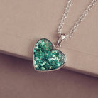 A small heart pendant, in sterling silver, filled with green crystals and cremation ashes, covered with resin