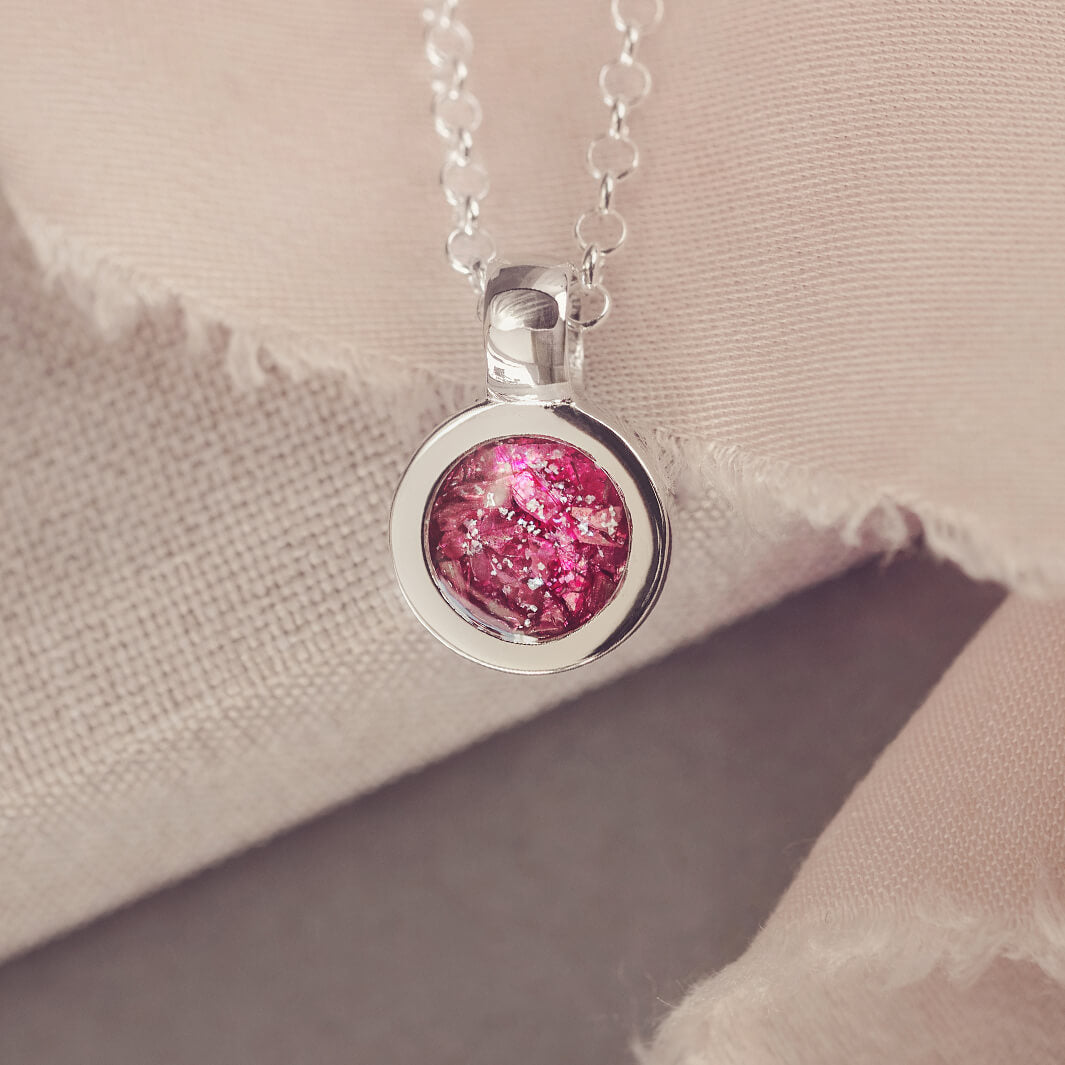 Sterling silver round necklace with a central section filled with memorial ashes and pink crushed crystals, displayed on a beige background