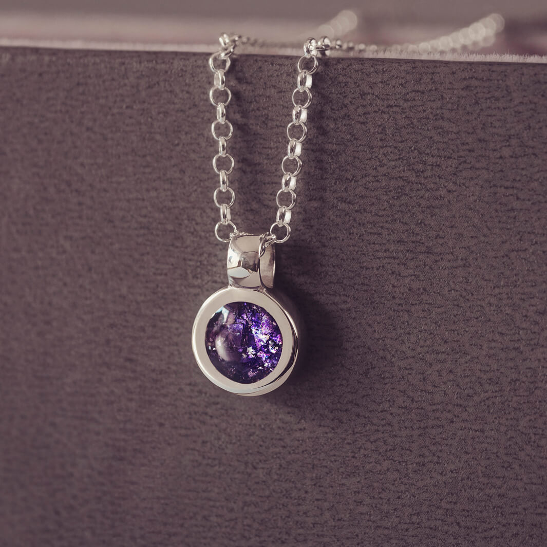 Sterling silver round necklace with a central section filled with memorial ashes and purple crushed crystals, displayed on a grey background