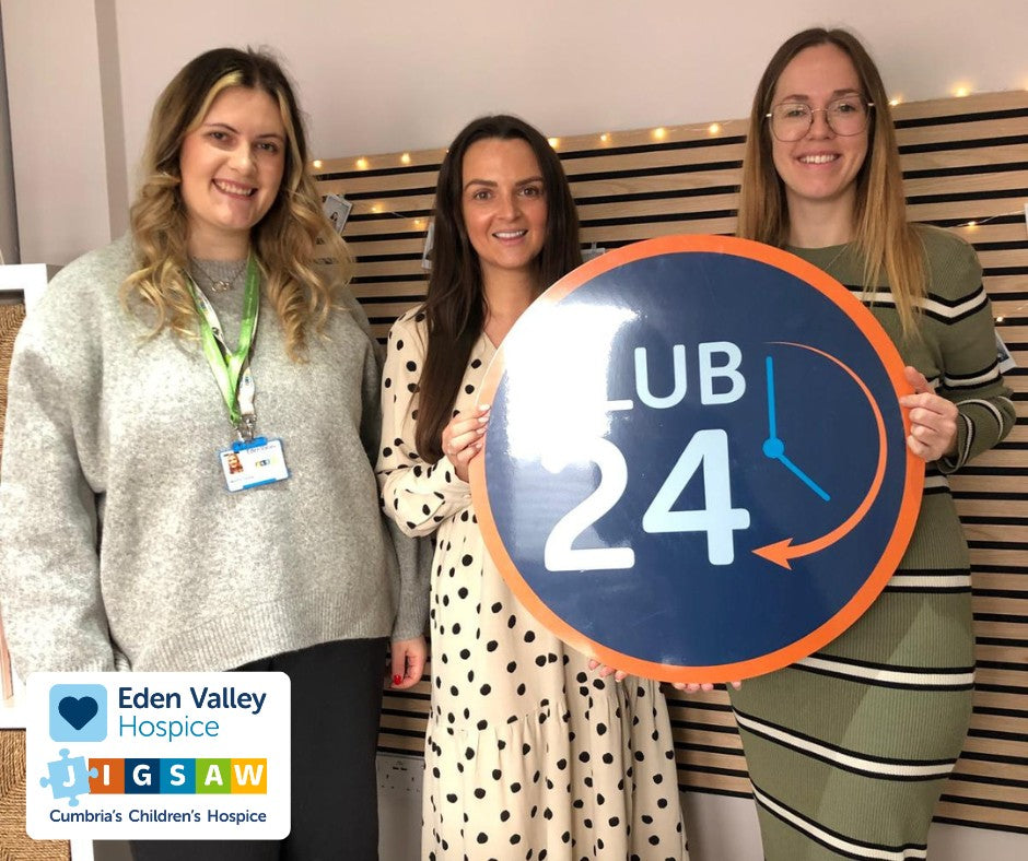 Two team members being presented with Club 24 sign from Eden Valley Hospice representative