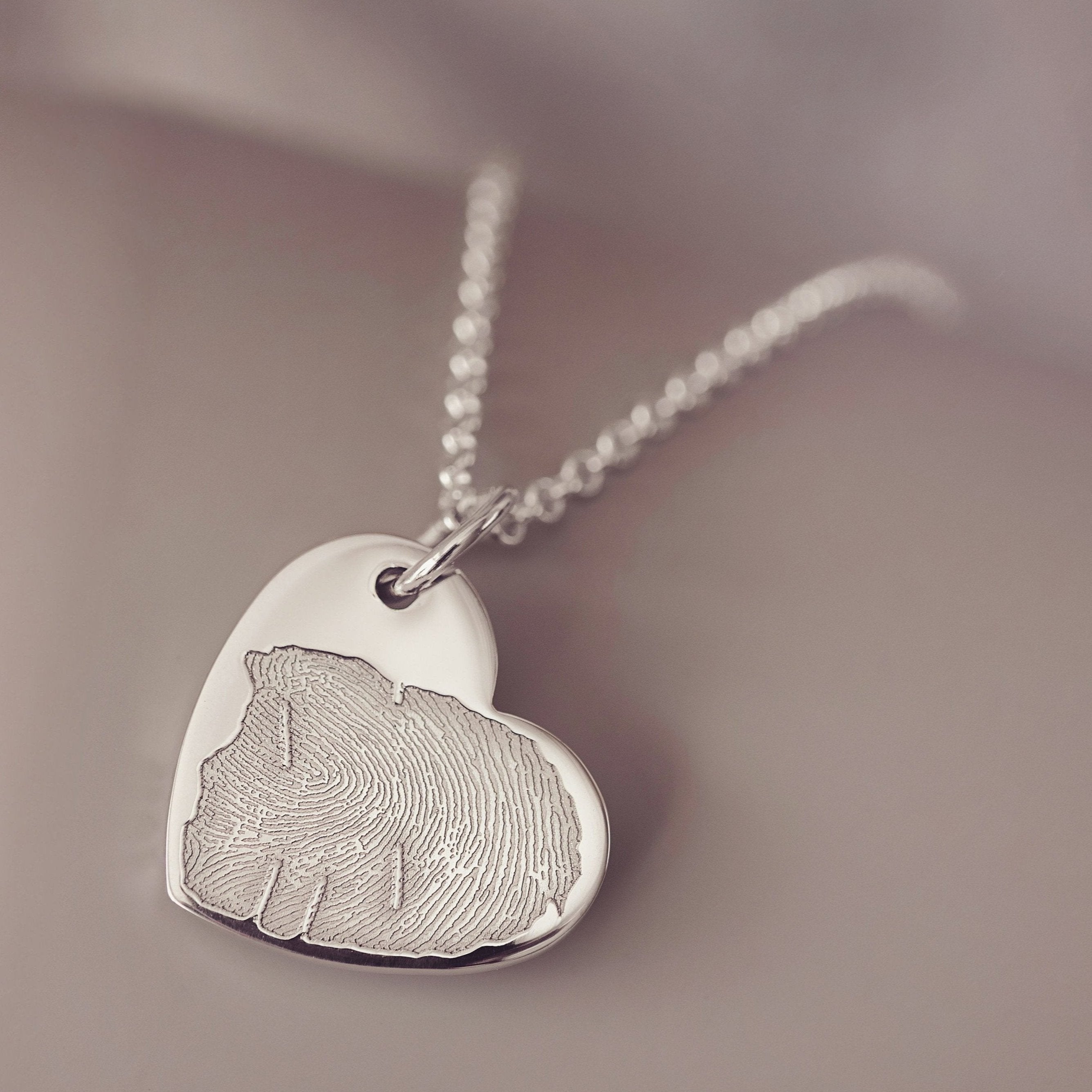 A close up of a heart-shaped necklace intricately engraved with a detailed fingerprint