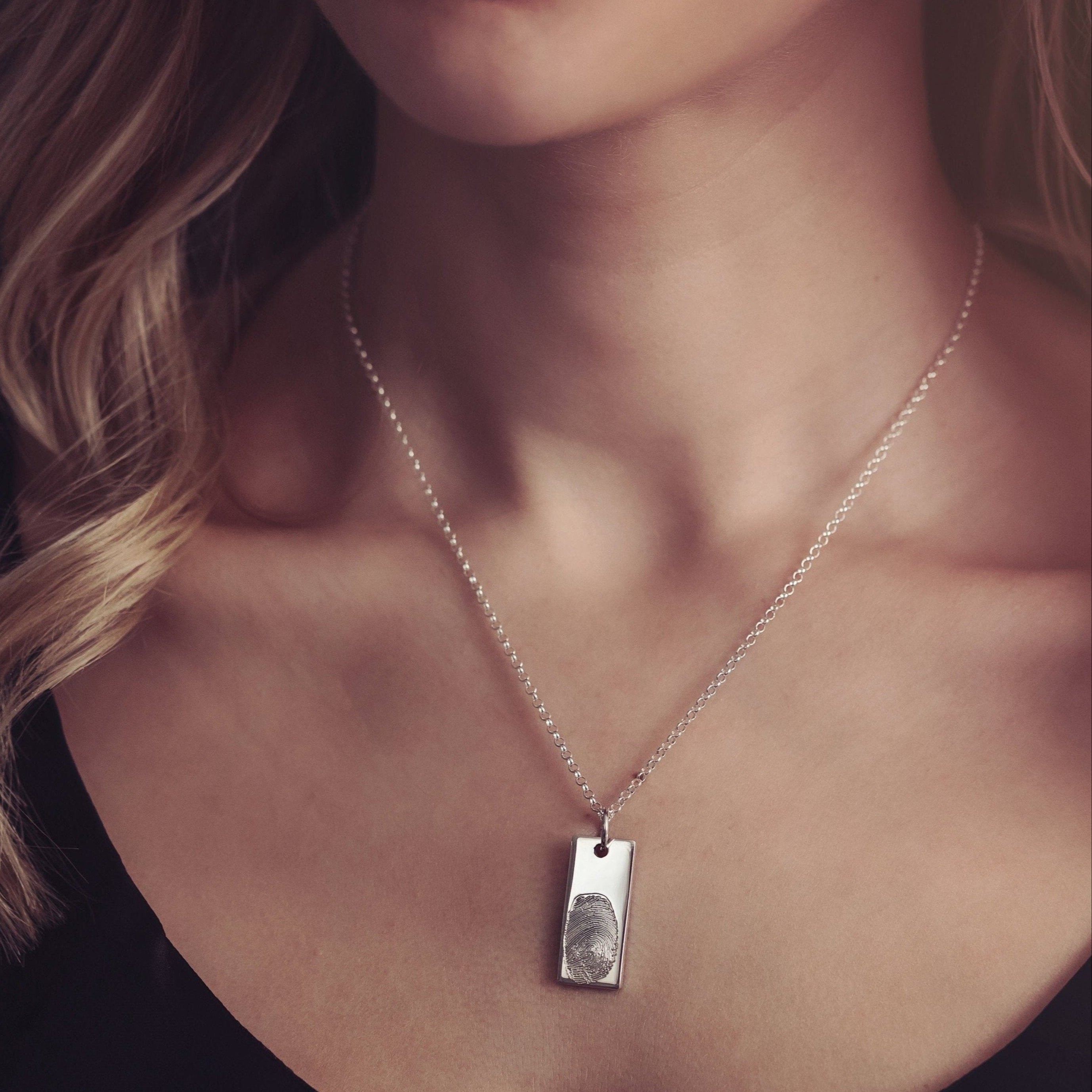 A woman with blonde hair elegantly wearing a silver tag fingerprint necklace with a black top