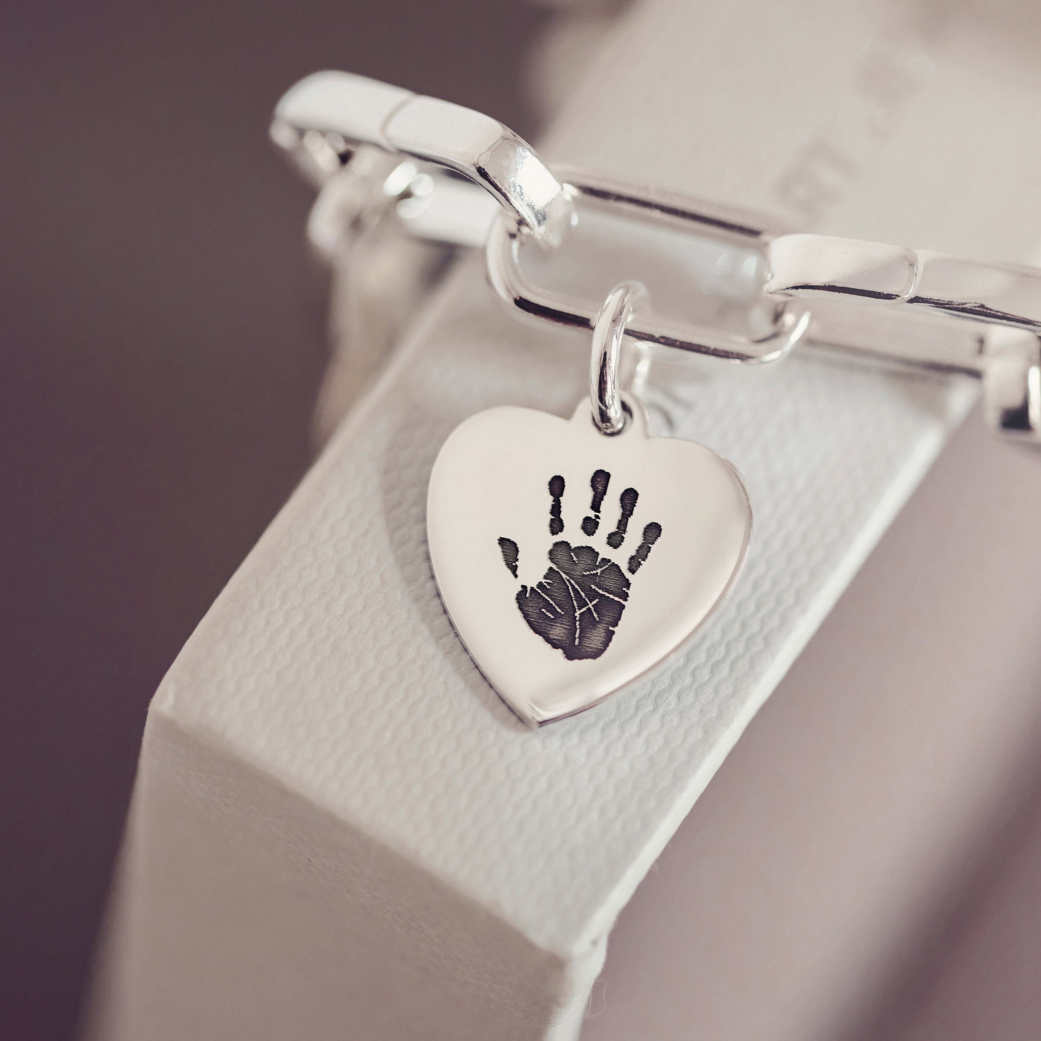 A silver collection bracelet with a heart charm featuring a handprint