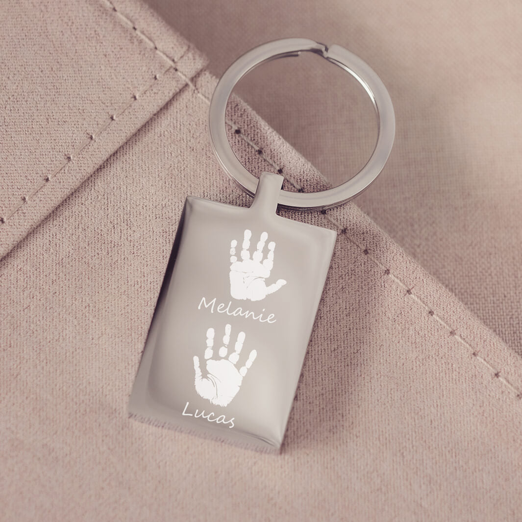 A stainless steel keyring, engraved with two handprints and names, on a pink fabric background