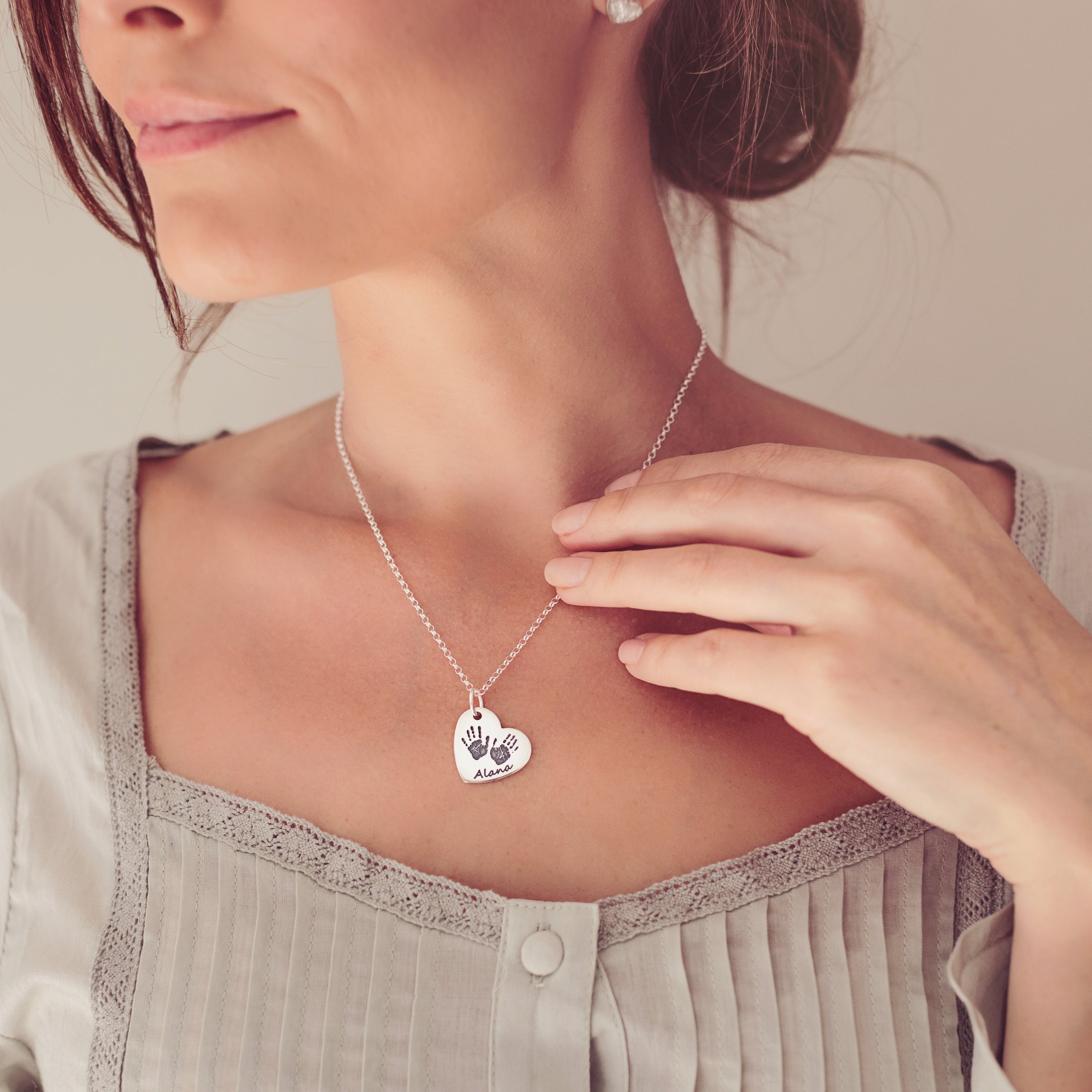 A woman elegantly wearing a heart shaped handprint necklace with name 'Alana' engraved