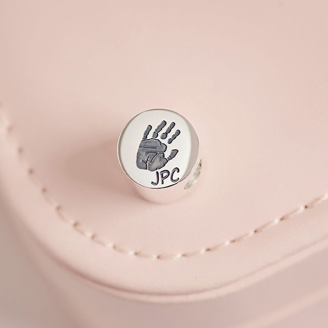 a round sterling silver charm bead, compatible with Pandora Bracelets, with a handprint and the initials JPC engraved into the front of the bead