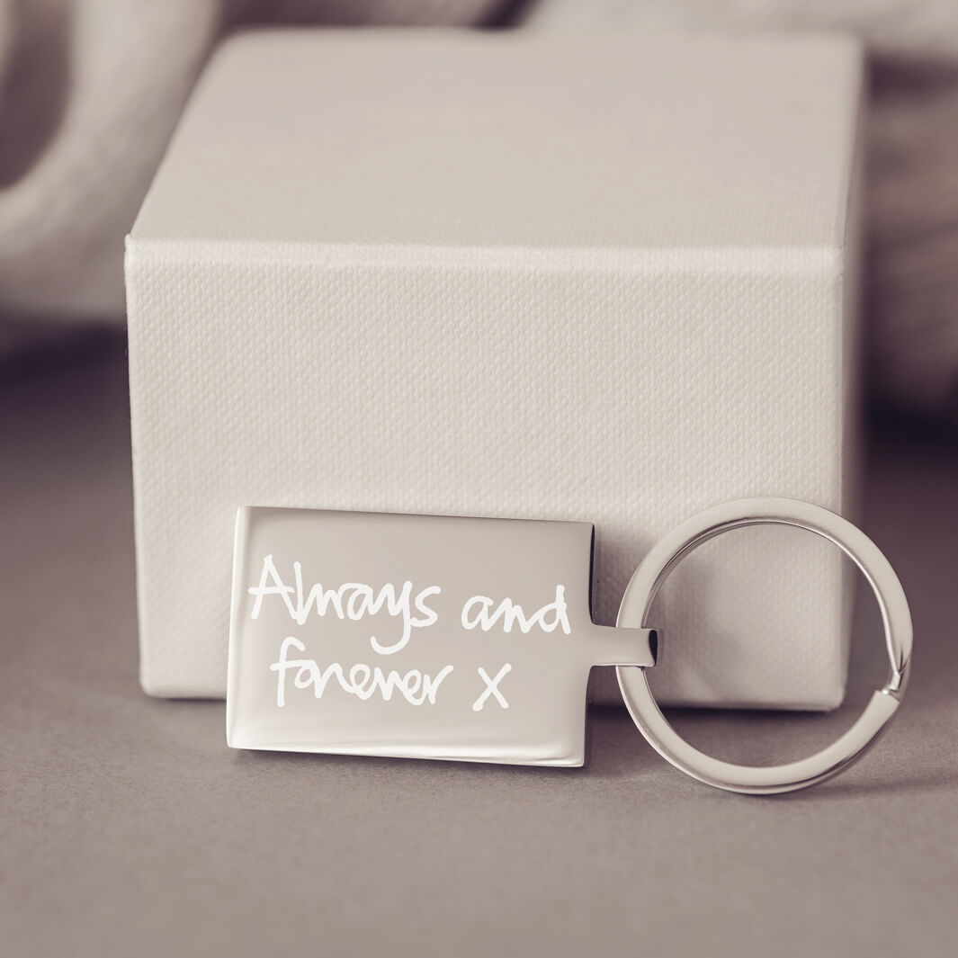 A stainless steel rectangular keyring, with a handwritten message of 'Always and forever x' engraved onto the front. Displayed against a light grey jewellery box.