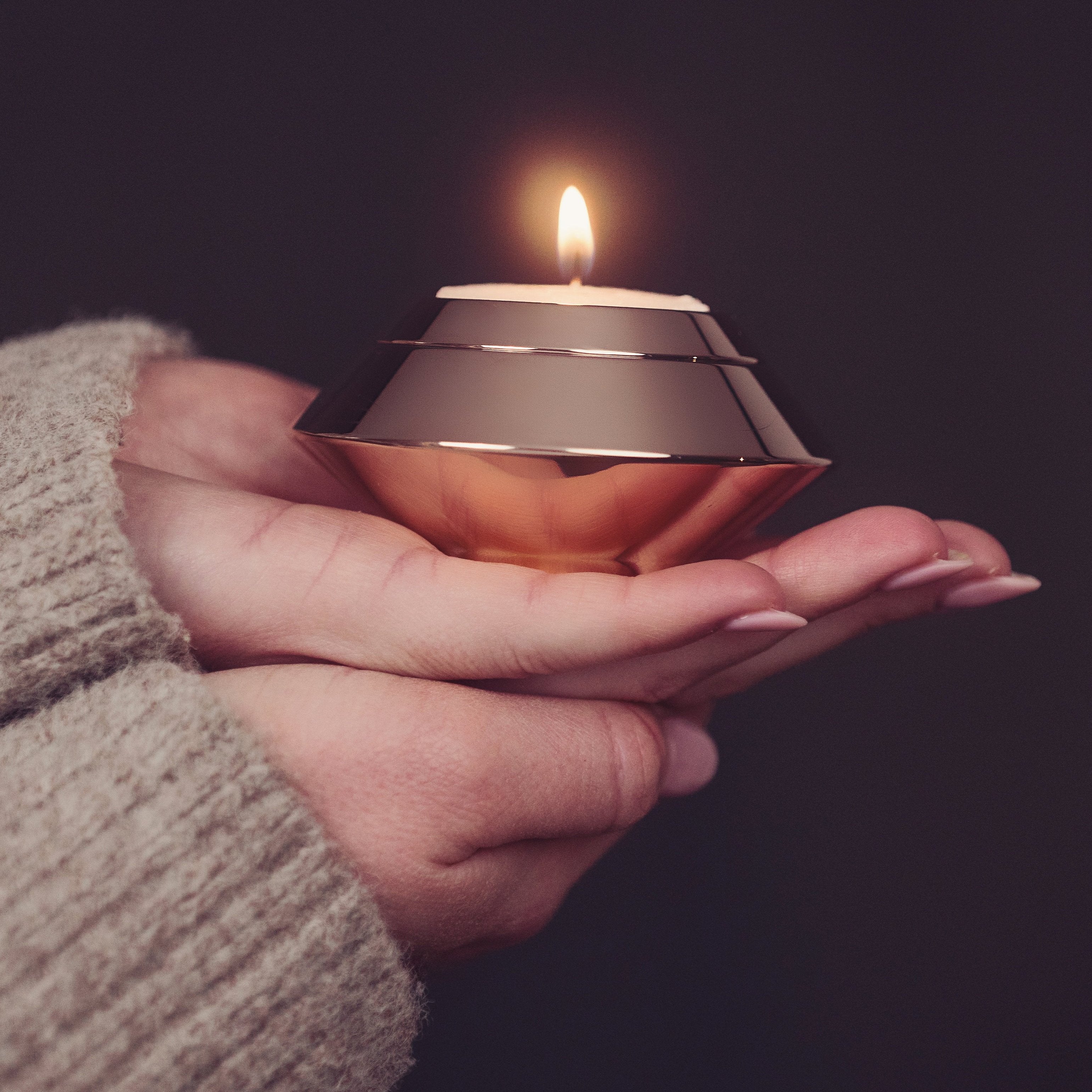 A close up of a woman holding a rose gold candle urn containing cremation ashes