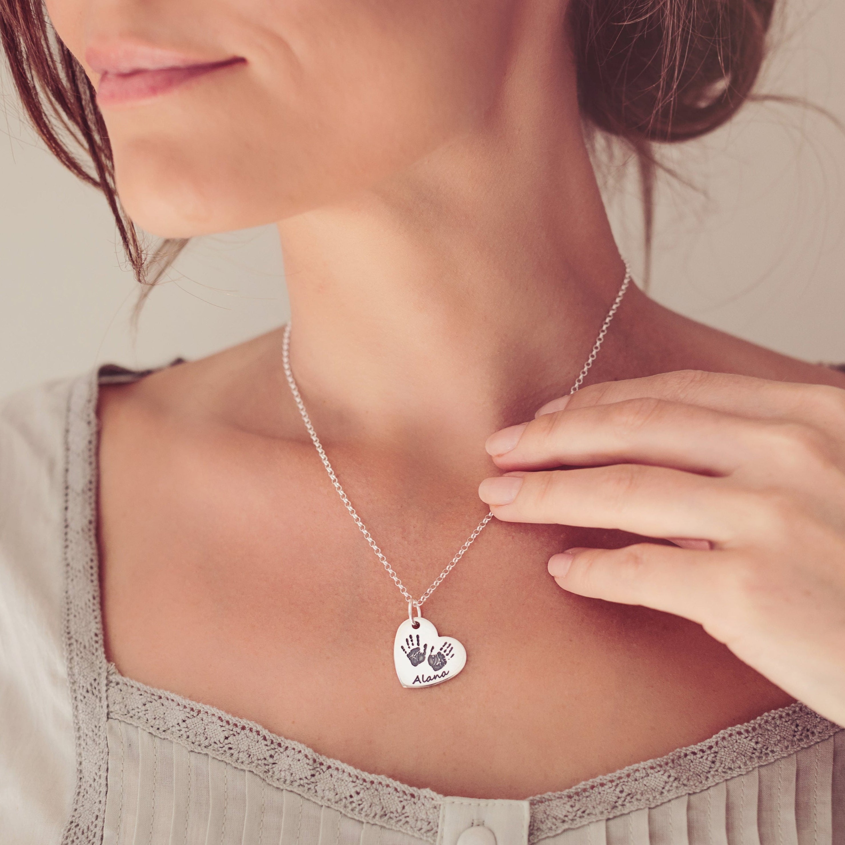 A woman wearing a silver heart necklace featuring two handprints and the name Alana