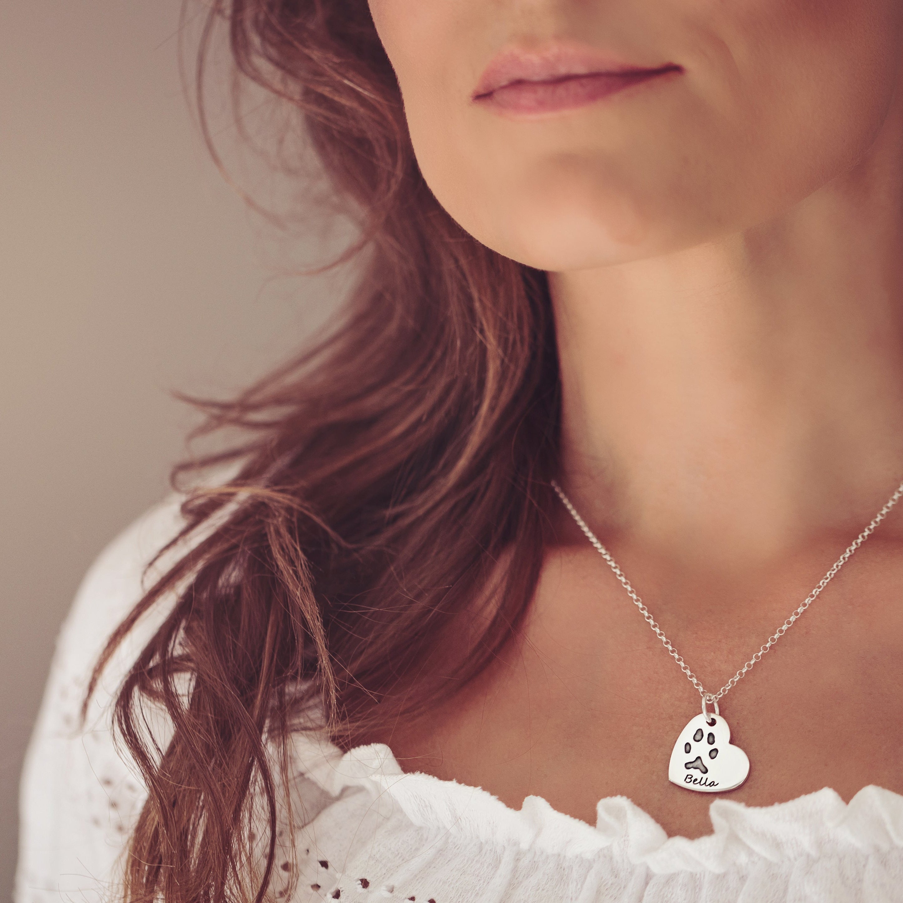 A close up of a woman wearing a heart necklace featuring Bella's pawprint and name