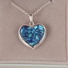 Sterling silver Large Heart necklace with a central section filled with memorial ashes and blue crushed crystals, displayed on a beige background.