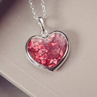 A sterling silver large heart pendant, hanging on a sterling silver belcher chain. The centre of the heart is filled with red crystal and ashes.