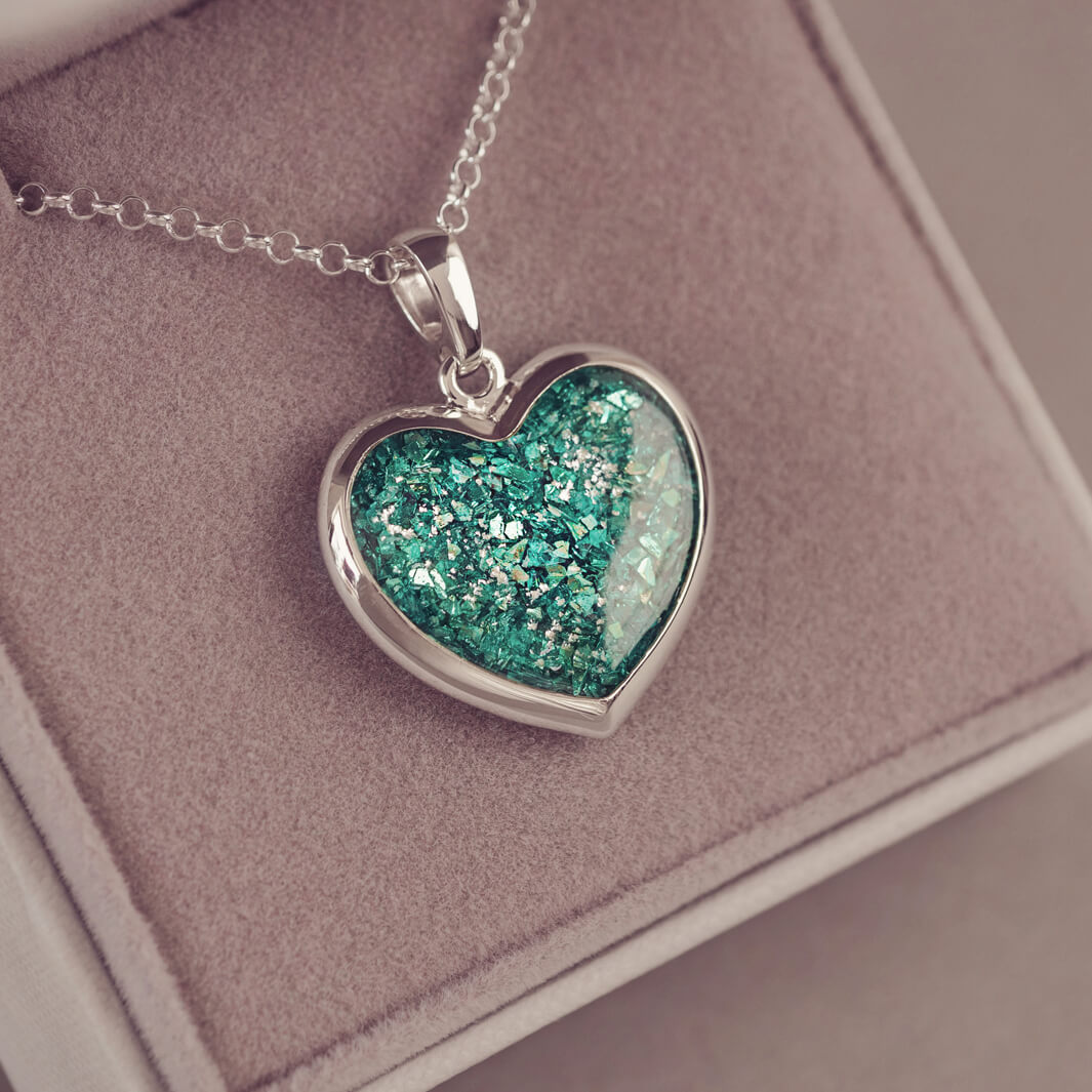 Sterling silver Large Heart necklace with a central section filled with memorial ashes and green crushed crystals, displayed in a grey jewellery box