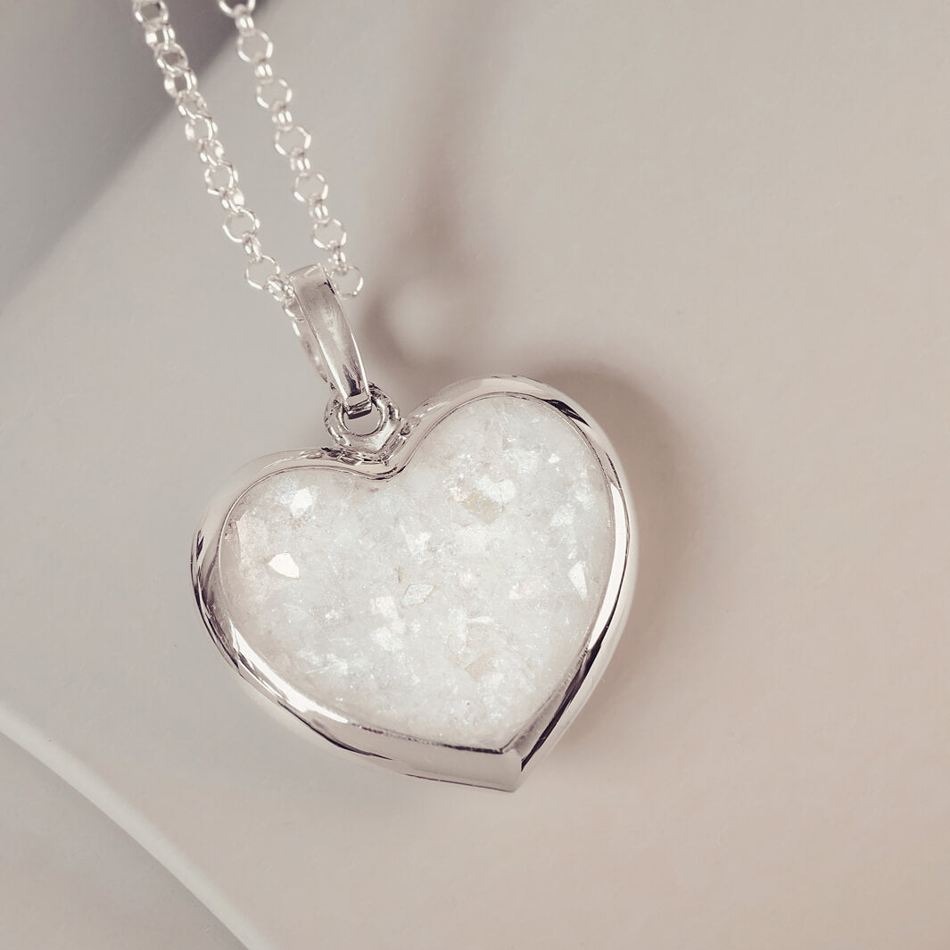 Sterling silver Large Heart necklace with a central section filled with memorial ashes and clear crushed crystals, displayed on a pale pink background.