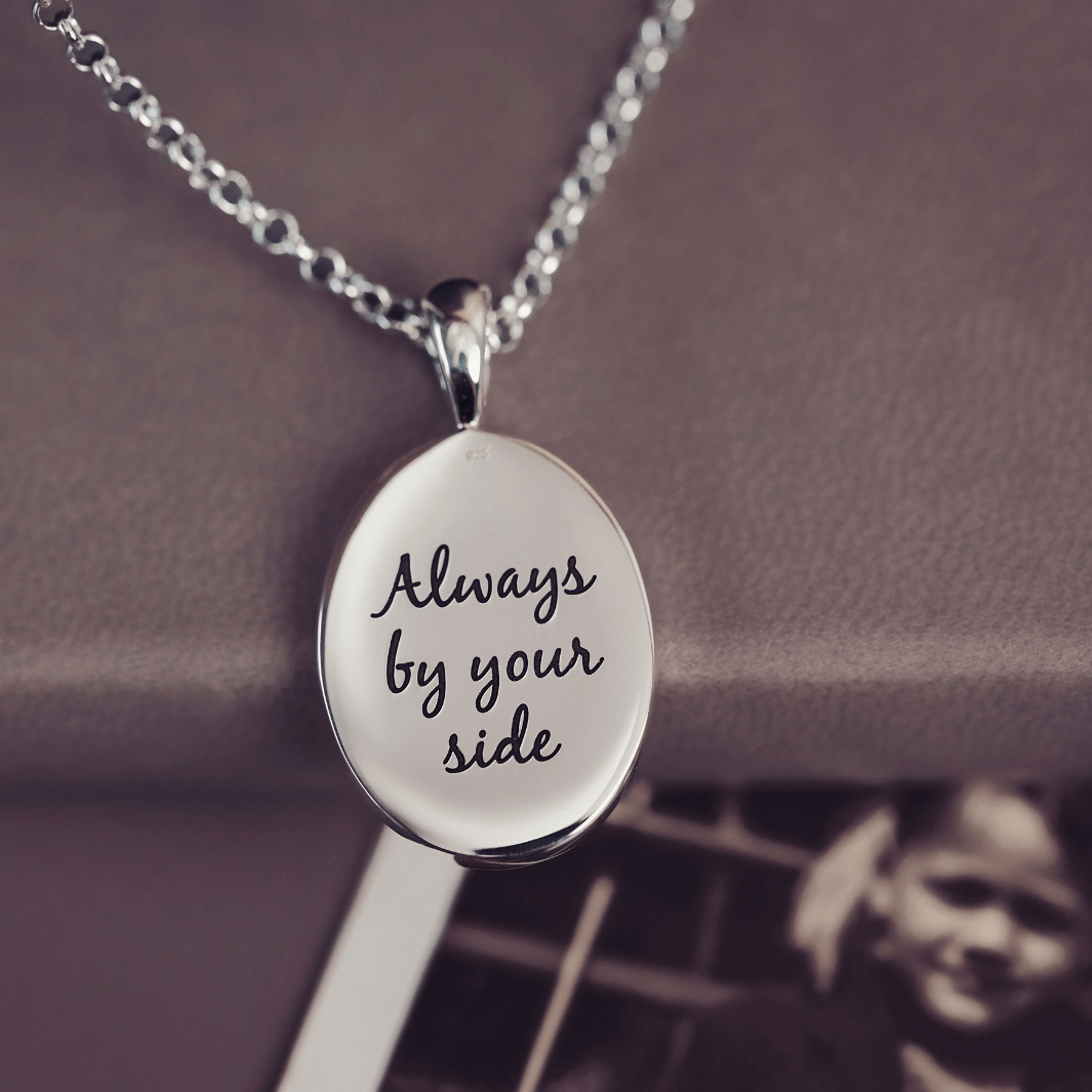 The reverse of a sterling silver Cremation Ashes Oval Necklace which has a message reading 'Always by your side' engraved into the pendant