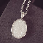 Sterling silver oval necklace with a central section filled with memorial ashes and white and clear crushed crystals, displayed in a grey jewellery box