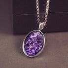 Sterling silver oval necklace with a central section filled with memorial ashes and purple crushed crystals, displayed on a grey jewellery box