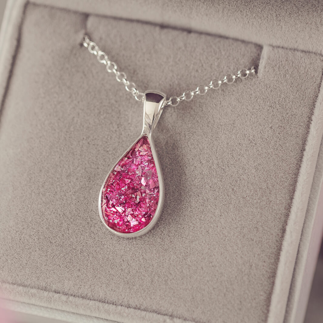 Sterling silver teardrop necklace with a central section filled with memorial ashes and pink crushed crystals, displayed in a grey jewellery box