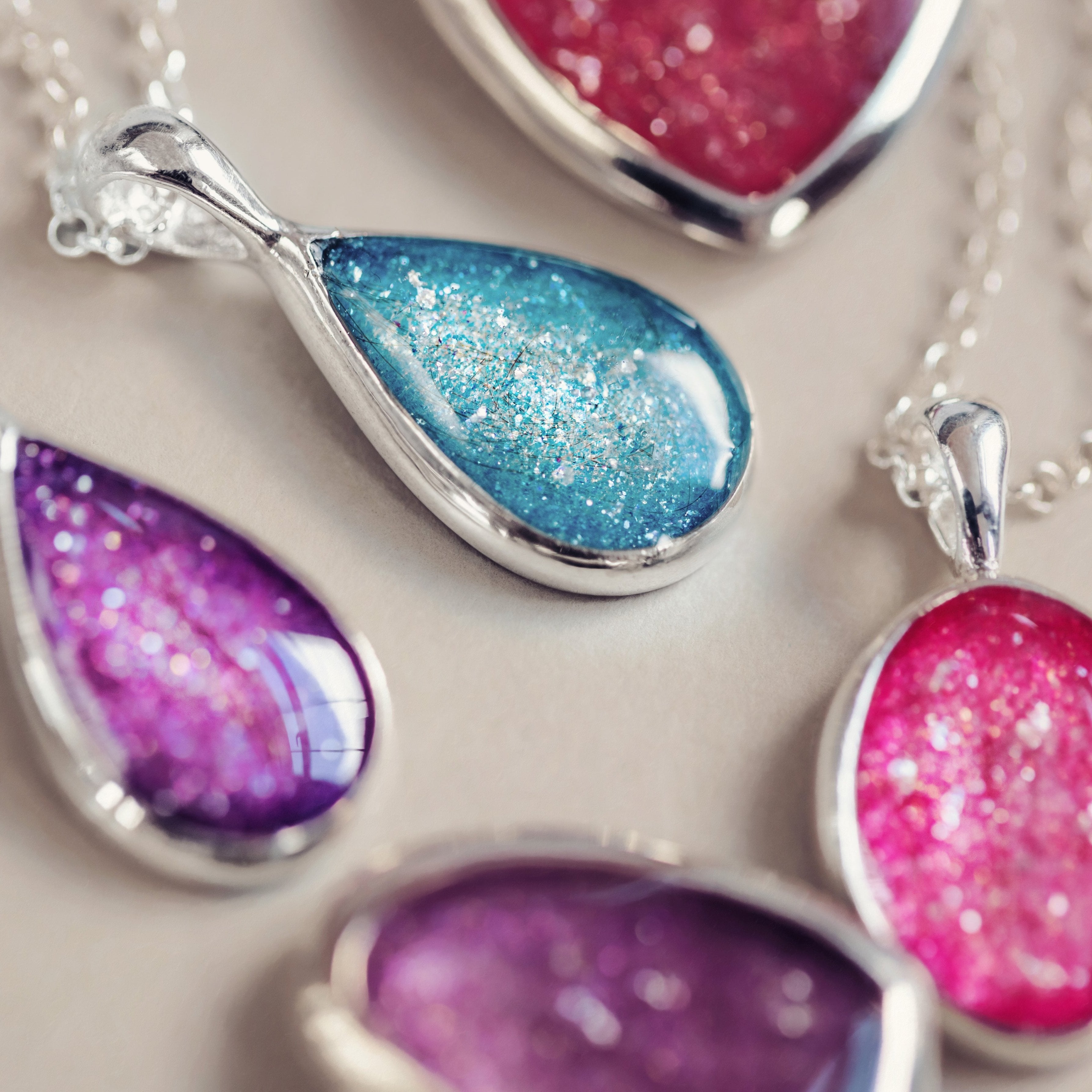 Collection of memorial hair pendants displayed on silver chains, showcasing a variety of colours and designs