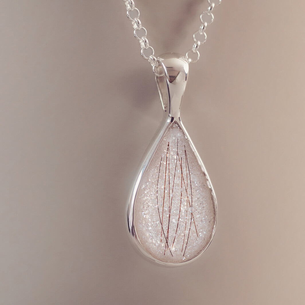 A silver teardrop necklace, filled with white glitter and strands of hair