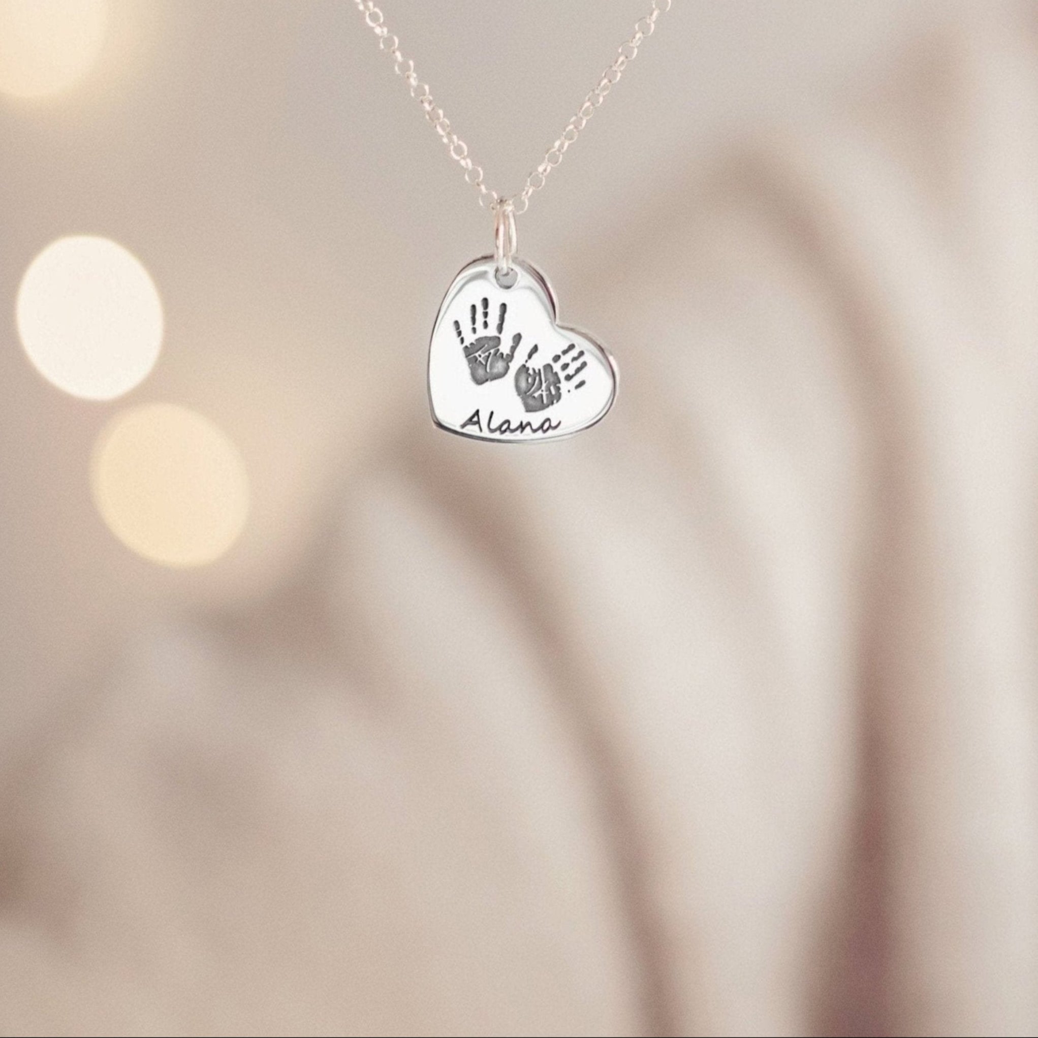 A woman delicately holding a heart necklace showing Alana's handprints and name